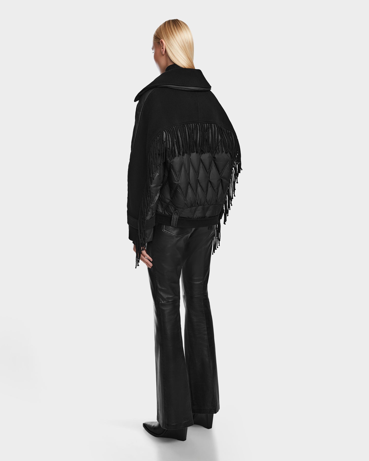 A person with long blonde hair wears the Rudsak ZOLA - 8124712 Black jacket, standing and facing away from the camera against a plain white background.