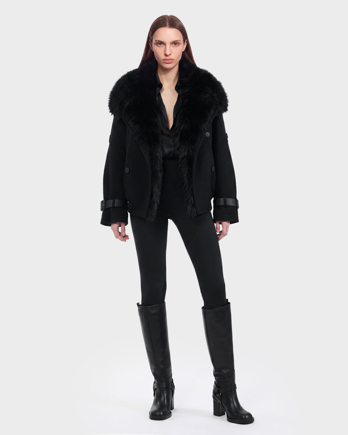 A person with long hair is wearing the Rudsak MAEMI - 8126985 Black wool down jacket featuring a removable faux fur collar, paired with a black shirt, black pants, and knee-high black boots, standing against a plain light gray background.