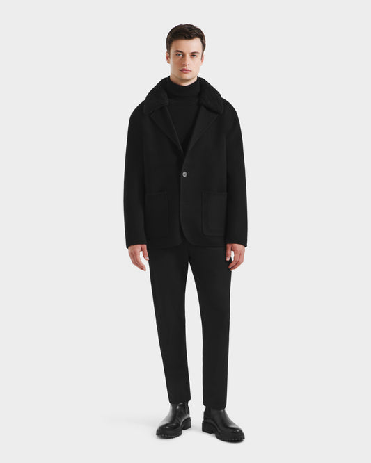 A man faces forward against a white background, wearing Rudsak’s AIDEN - 6125558 Black men’s wool-blend coat over a black turtleneck, paired with black pants and shoes for a refined outerwear look.