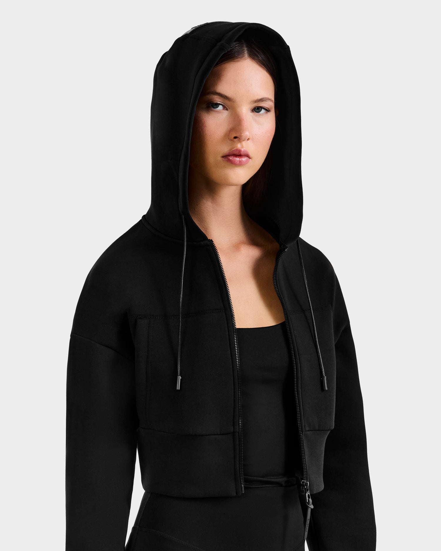 A woman with straight brown hair models the Rudsak ALAYA - 8525038 Black women’s hoodie, paired with a matching black top, capturing casual-chic loungewear style against a plain light gray background.
