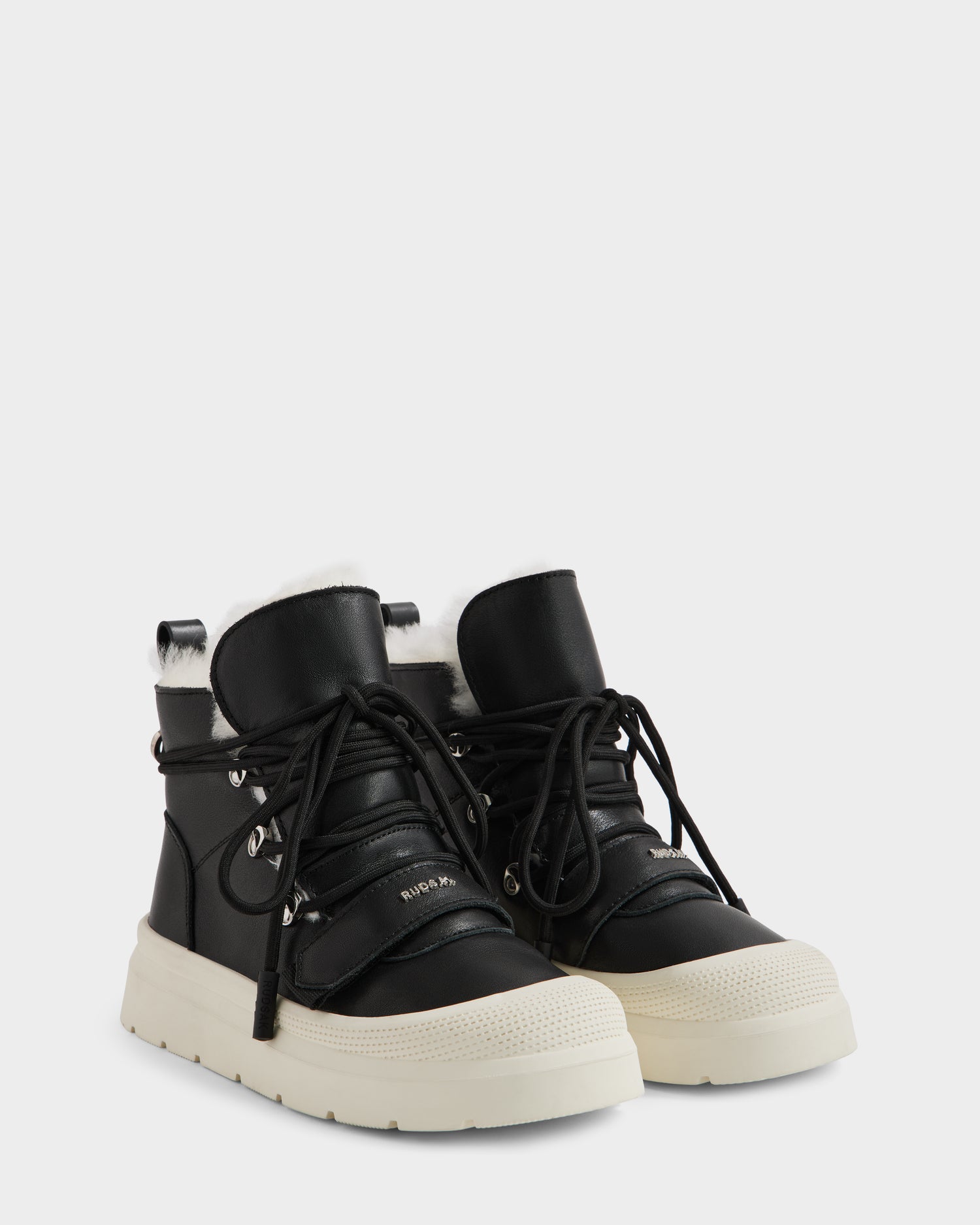 Rudsak’s ALEXEY L - L225518 Black high-top sneakers feature cozy wool lining, thick white rubber soles, black laces, and silver eyelets—a stylish winter boot photographed on a light gray background.