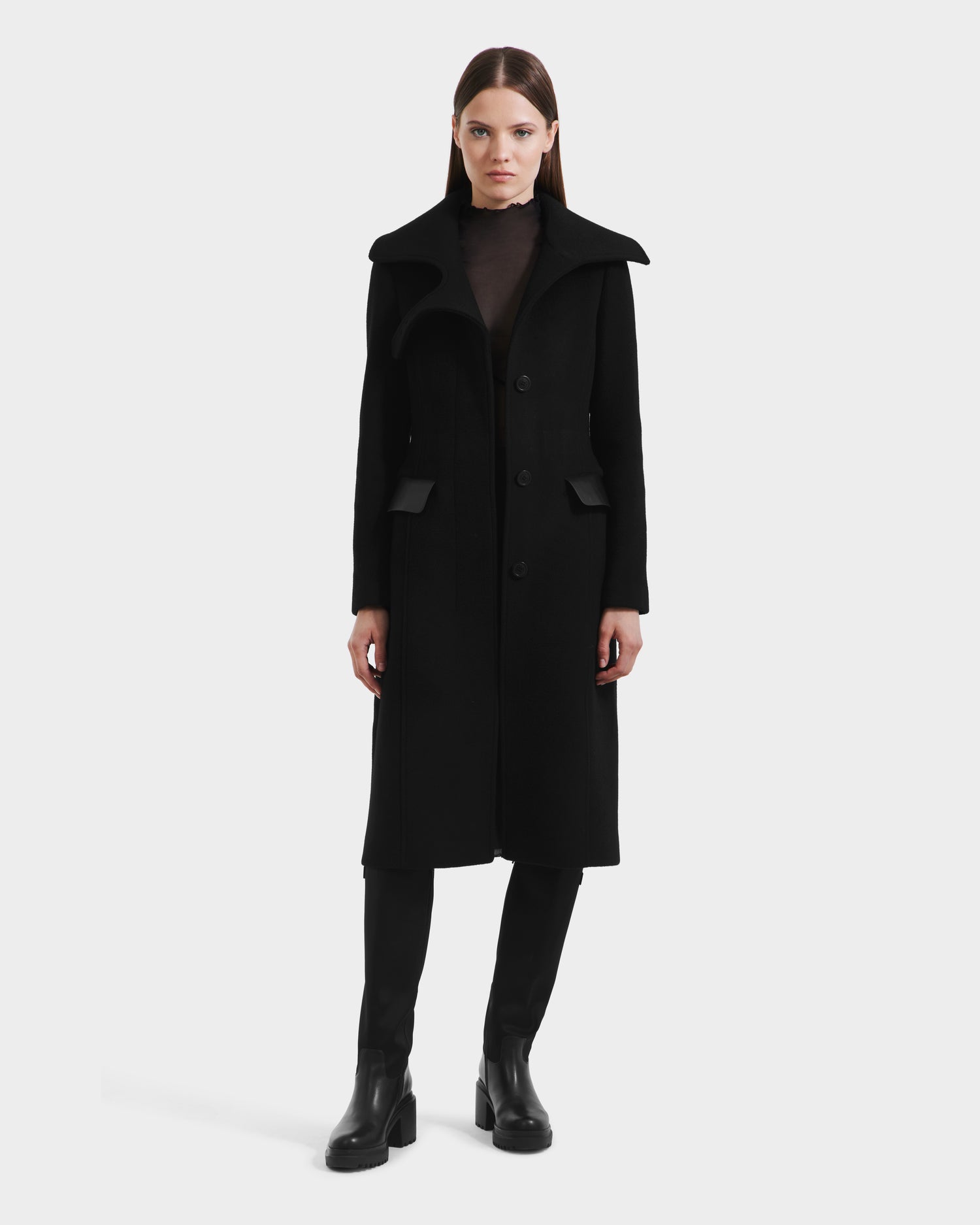 A woman faces forward against a white background, wearing the Rudsak ALICE - 8125606 Black womens wool coat with a wide collar, paired with black pants and boots.