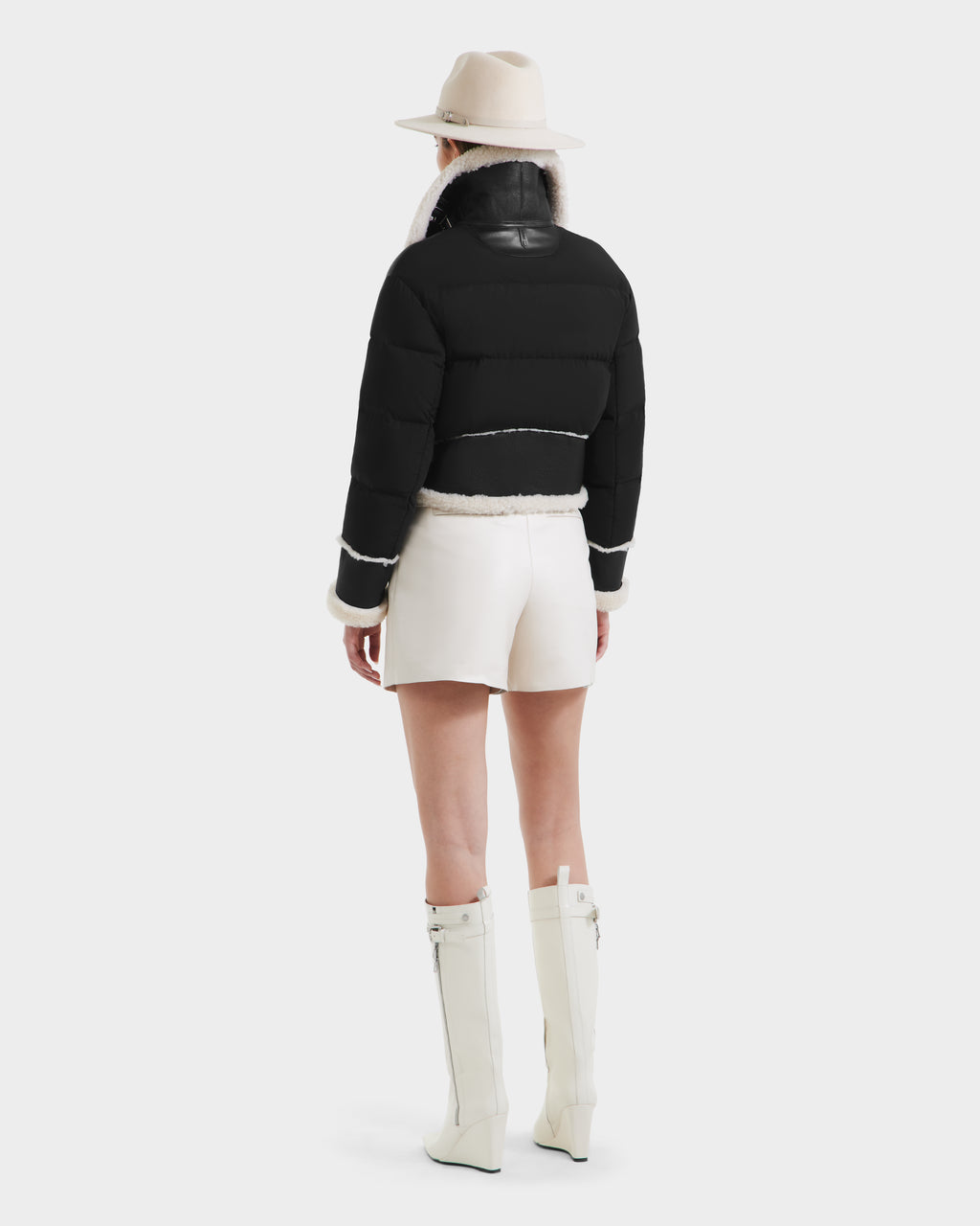 Someone wears the ANA - 8125508 Black jacket by Rudsak, white shorts, knee-high white boots, and a beige hat, standing with their back to the camera against a plain background.