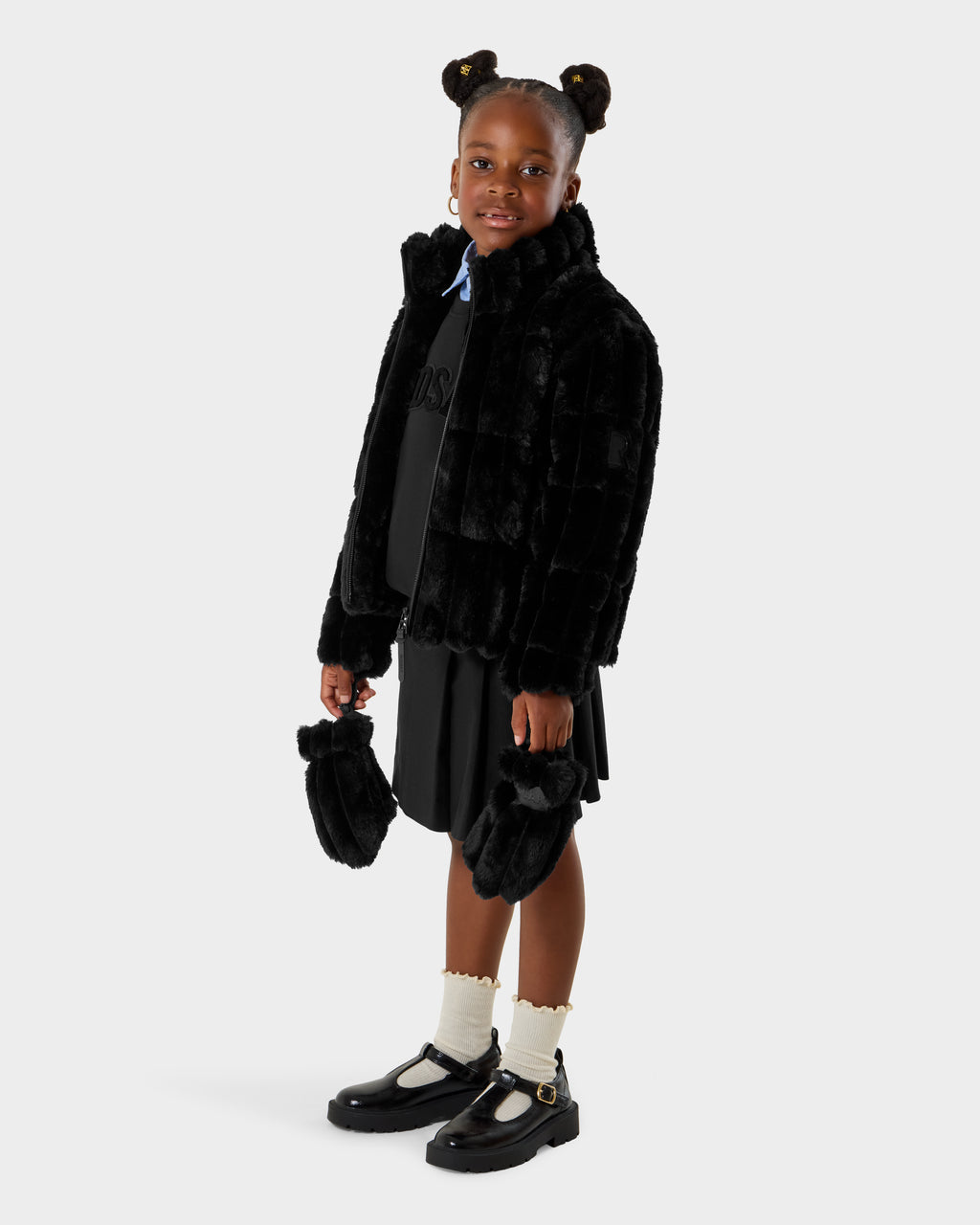 A young girl with two buns wears the Rudsak ANASTASIA K - 0125000 Black jacket and matching fur purse, paired with a black skirt, white socks, and black shoes. She smiles against a plain light background.