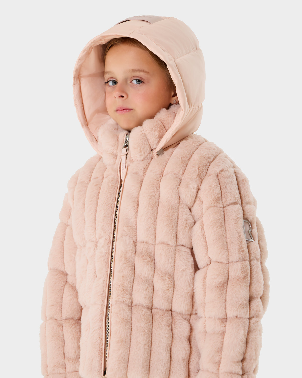 A young child wears the Rudsak ANASTASIA K - 0125000 quilted faux fur jacket in pastel pink, featuring a hood, while looking slightly to the side against a plain white background.