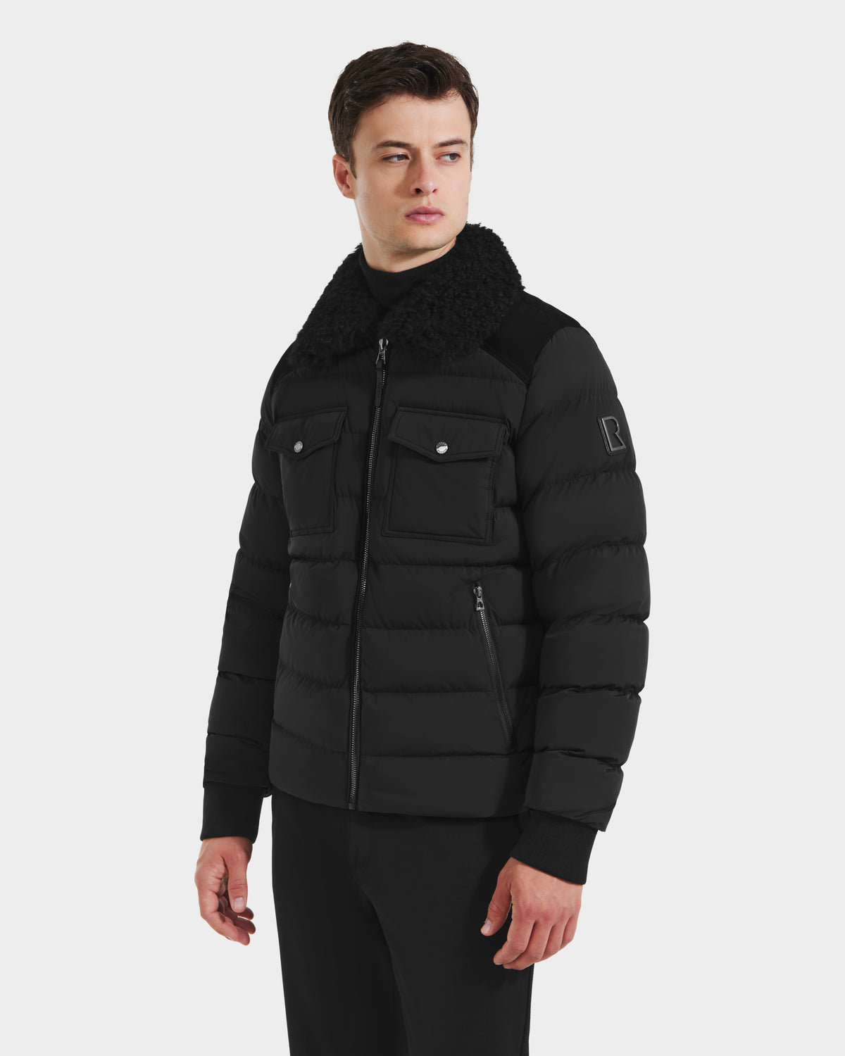 A man wearing the Rudsak ANTHONY - 6125042 Black mens aviator jacket with a shearling collar, front zip, and chest pockets stands against a plain white background, looking slightly to his left.