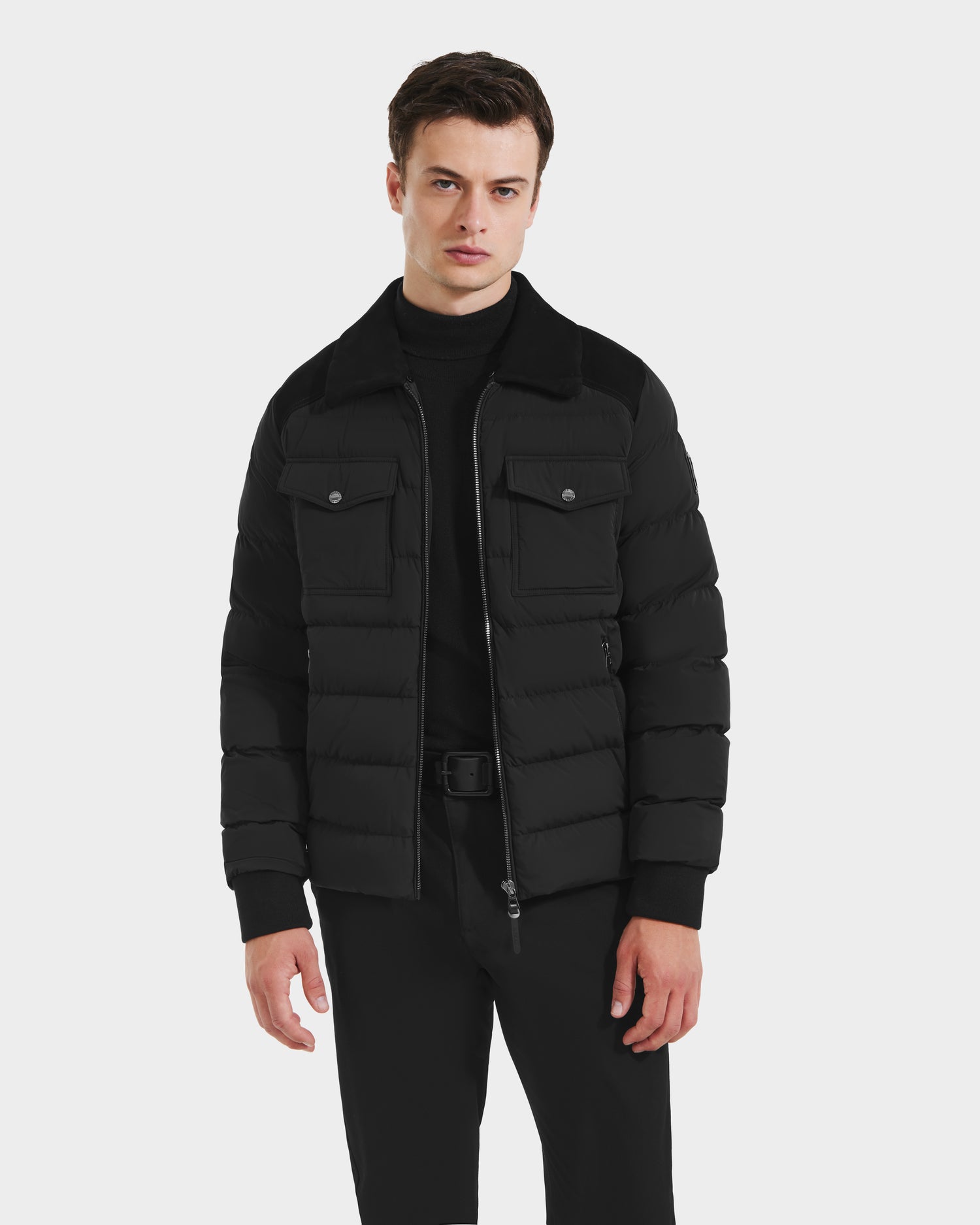 A man wearing the Rudsak ANTHONY - 6125042 Black quilted jacket over a black turtleneck and pants stands facing forward against a plain white background.