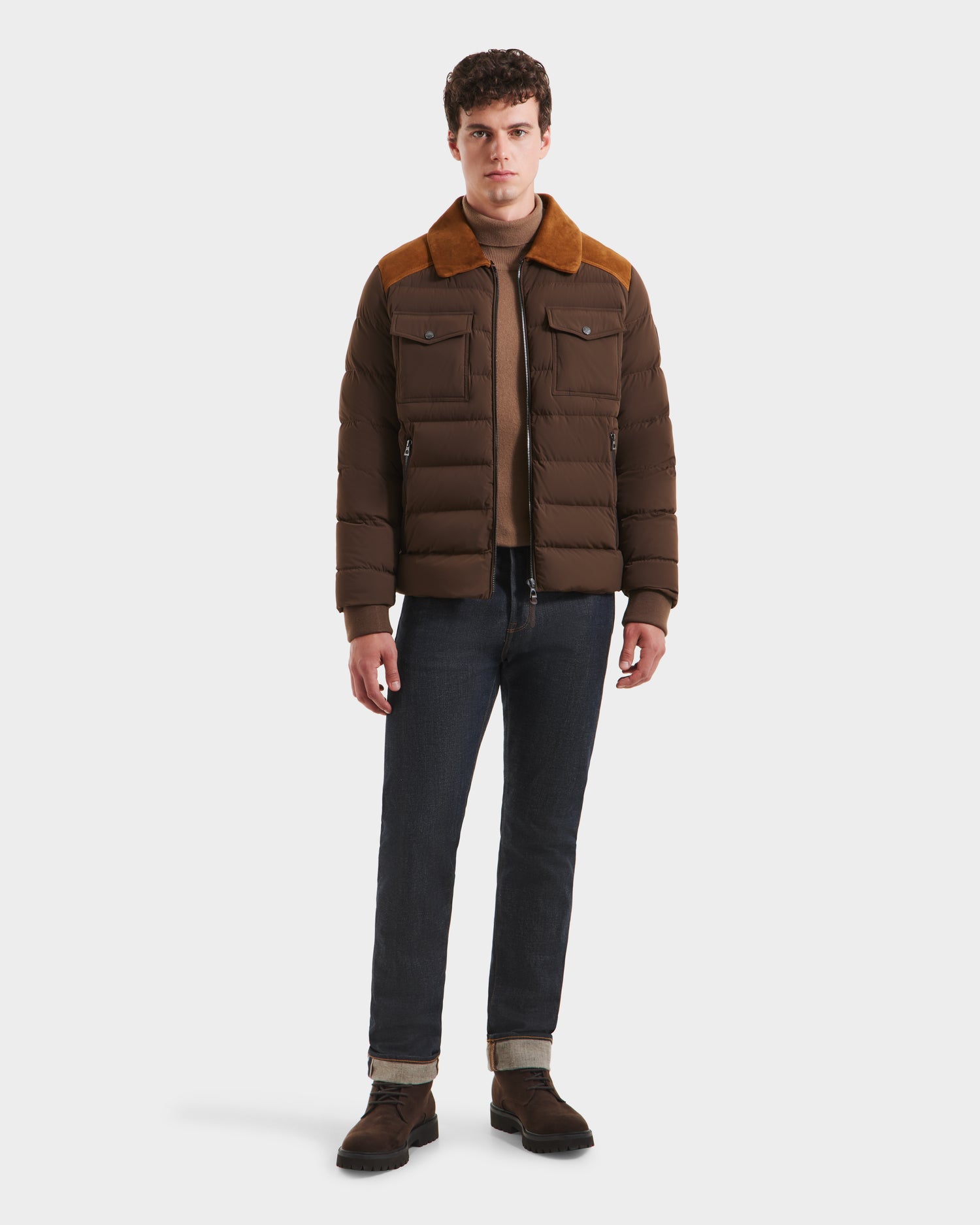 A man stands facing forward in the Rudsak ANTHONY - 6125042 Mocha brown quilted jacket with corduroy collar, paired with a brown sweater, dark jeans, and brown boots. The background is plain white.