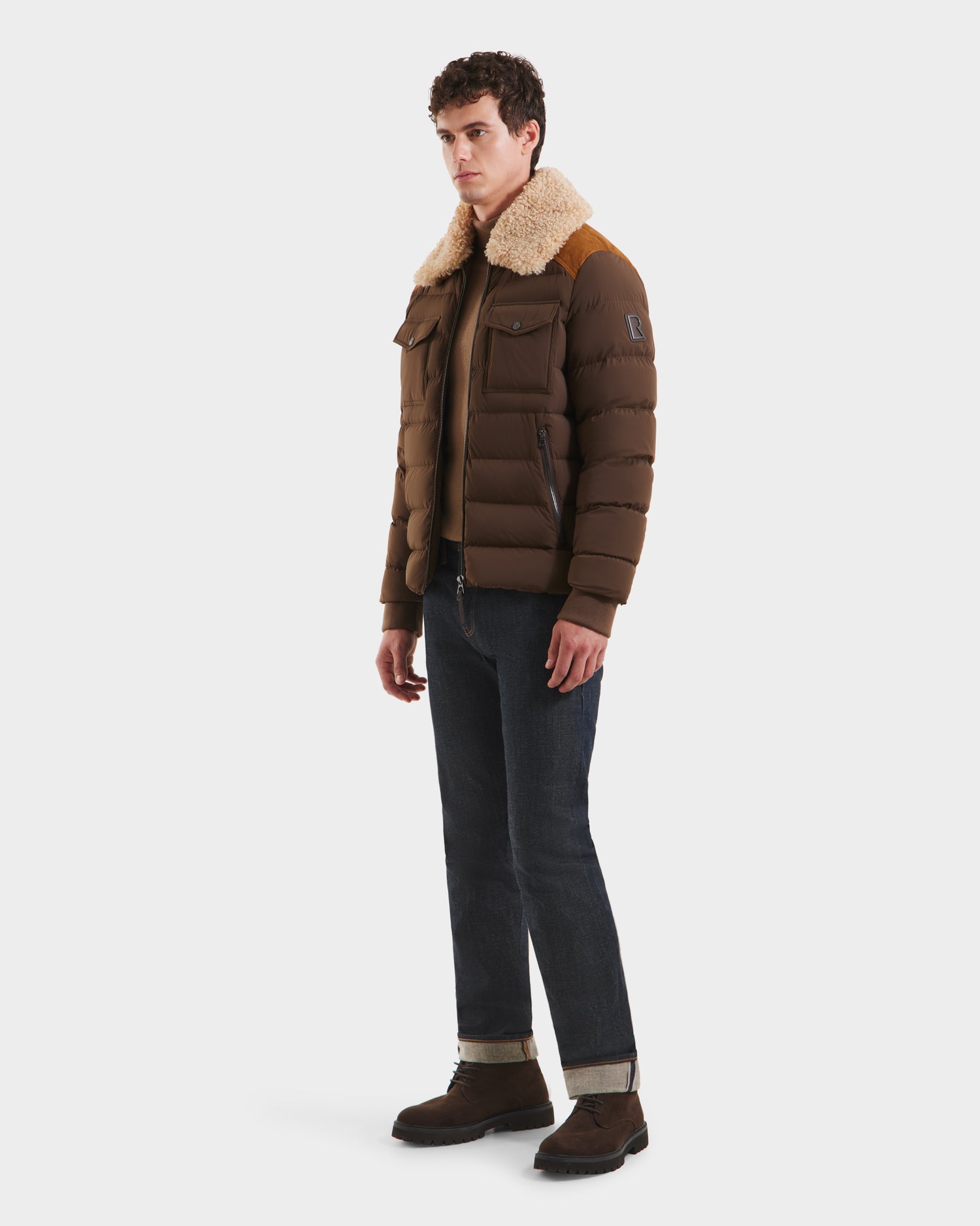 A man wears the Rudsak ANTHONY - 6125042 Mocha men’s aviator jacket with a shearling collar, styled with dark jeans and brown boots against a plain white background.