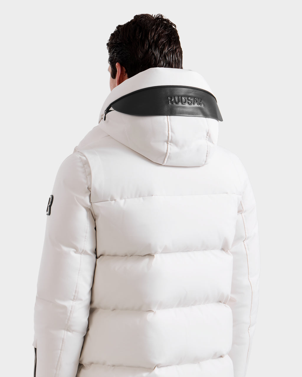 A person seen from the back wears the APOLLO H - 6125690 Vanilla by Rudsak, a white quilted parka with black hood trim. The winter jacket displays "RUDSAK" on the hood and a logo on the sleeve, set against a plain white background.