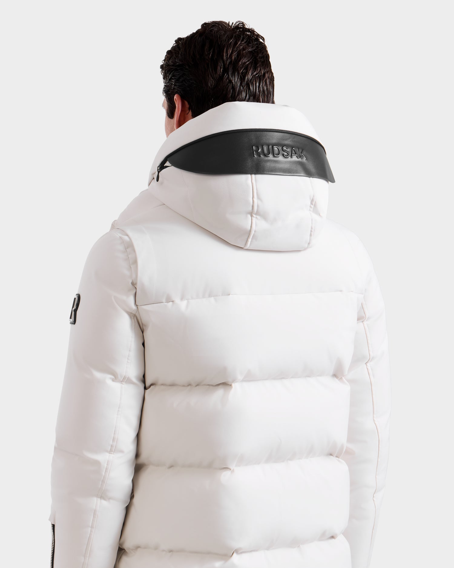 A person seen from the back wears the APOLLO H - 6125690 Vanilla by Rudsak, a white quilted parka with black hood trim. The winter jacket displays "RUDSAK" on the hood and a logo on the sleeve, set against a plain white background.
