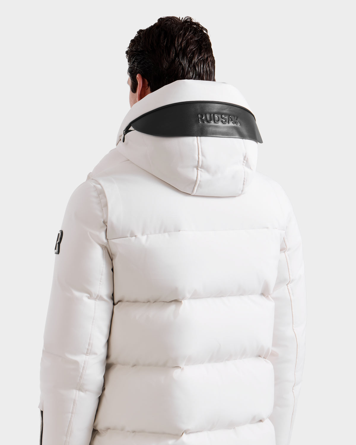 A person seen from the back wears the APOLLO H - 6125690 Vanilla by Rudsak, a white quilted parka with black hood trim. The winter jacket displays "RUDSAK" on the hood and a logo on the sleeve, set against a plain white background.