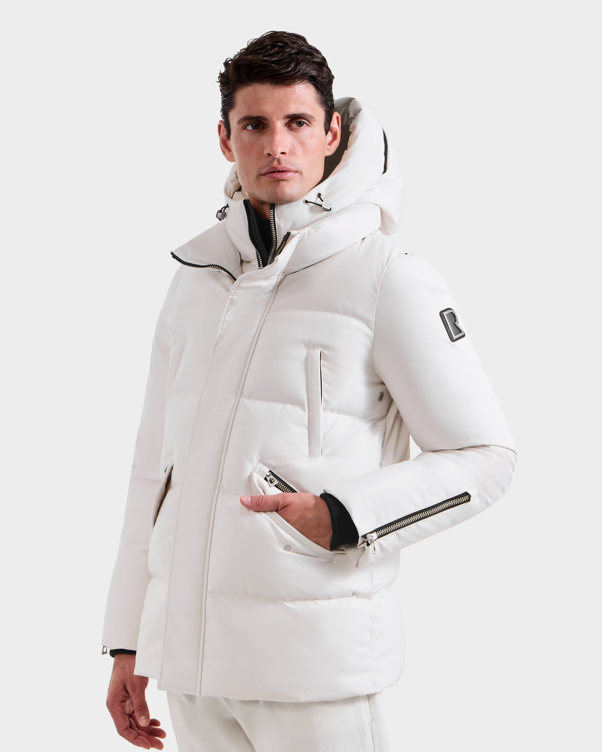 A man wears the Rudsak APOLLO H - 6125690 Vanilla men’s quilted down parka with zippered pockets and vegan leather trim, standing against a plain white background.
