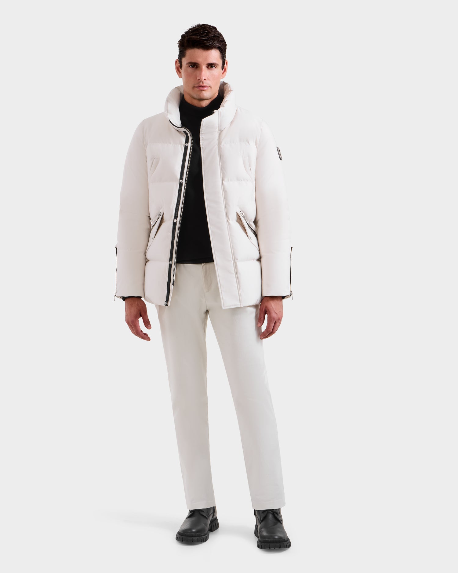 A man stands facing forward in the Rudsak APOLLO H - 6125690 Vanilla winter performance jacket and pants, paired with a black shirt and boots, set against a plain white background.