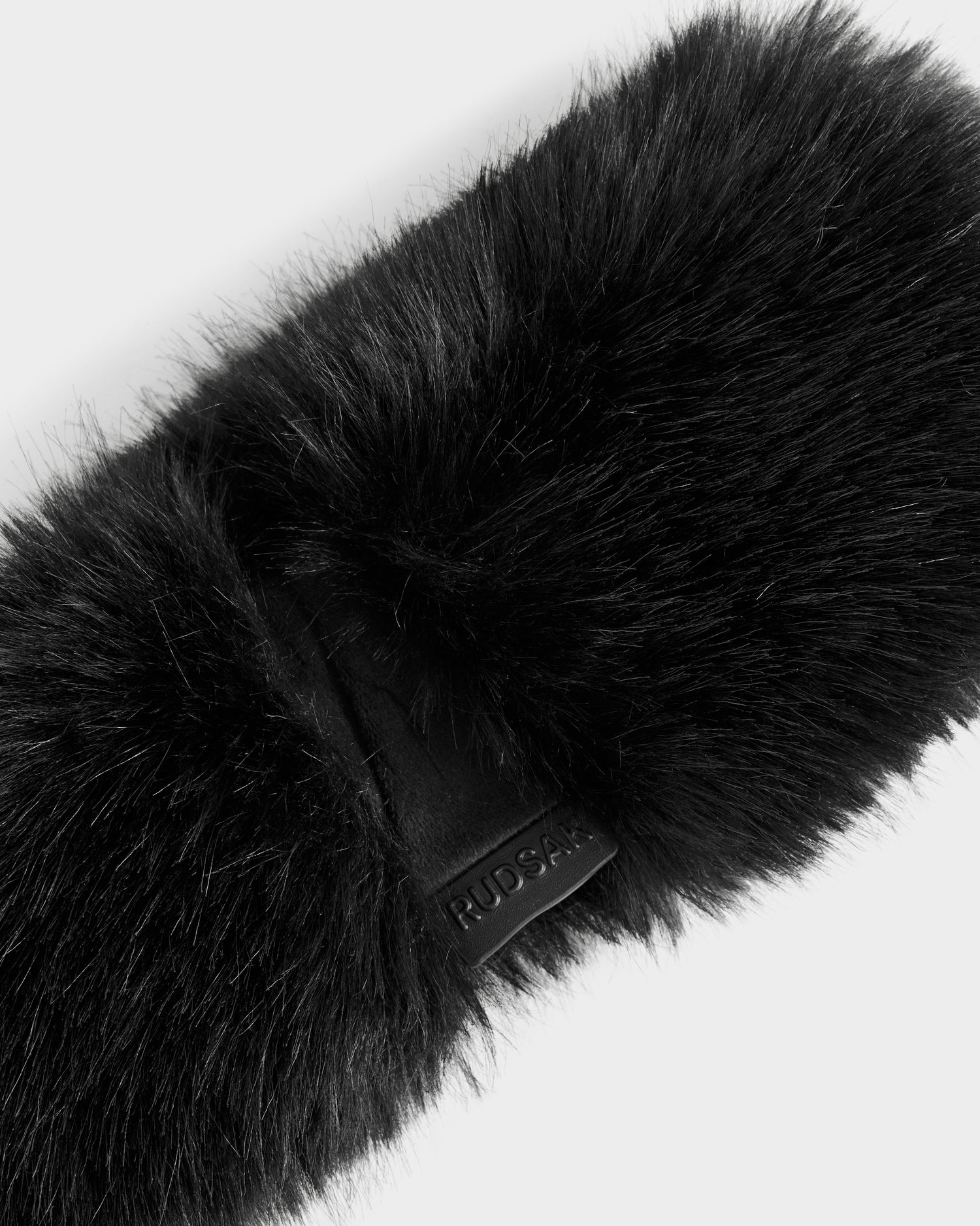 A close-up of the ARLETTE - 8425544 Black women's faux fur headband by Rudsak, featuring a small brand tag against a plain white background—a chic winter accessory ideal for cold-weather style.
