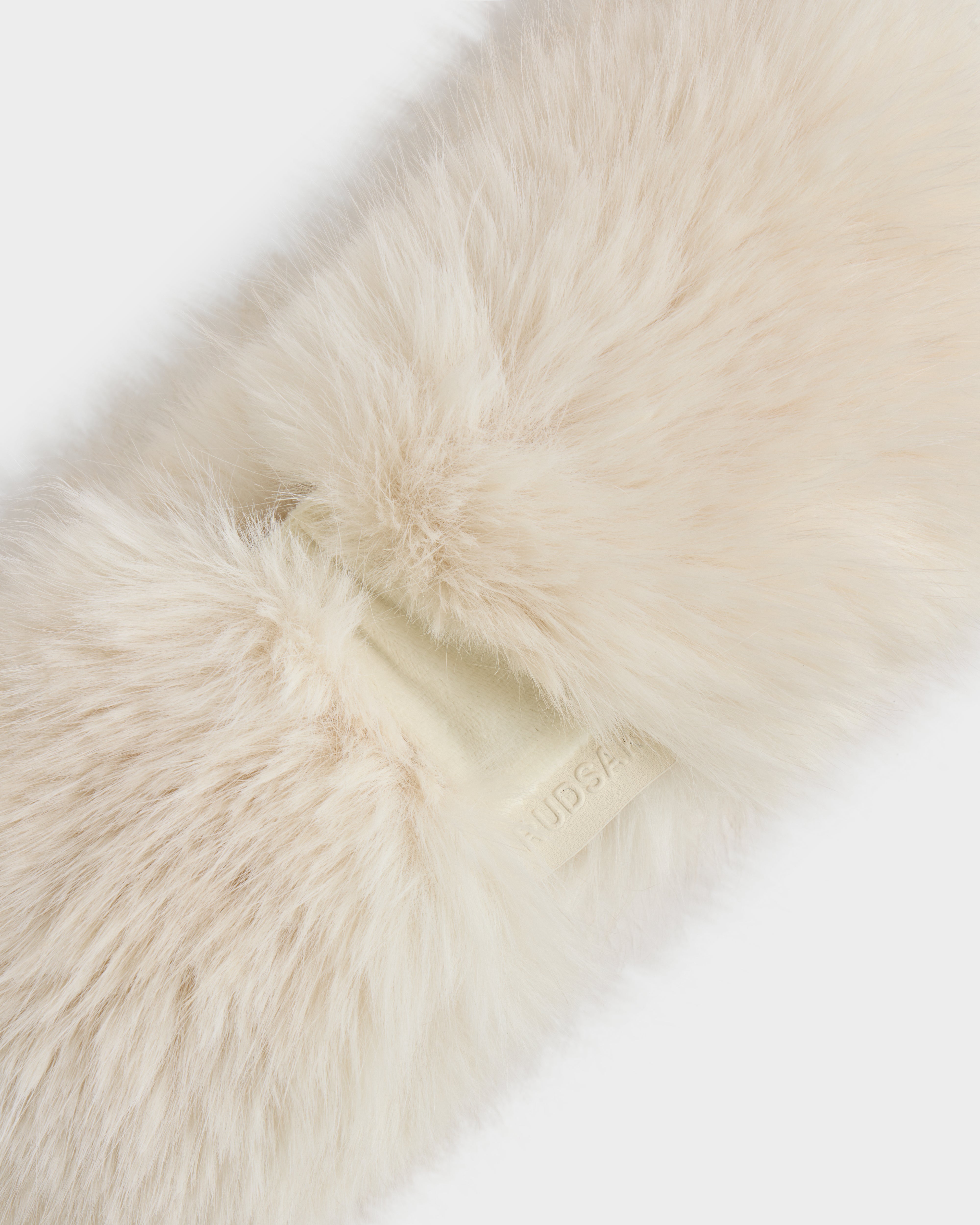 Close-up of the ARLETTE - 8425544 Vanilla women’s faux fur headband by Rudsak, a fluffy cream-colored winter accessory with a small, embossed tag partially visible.