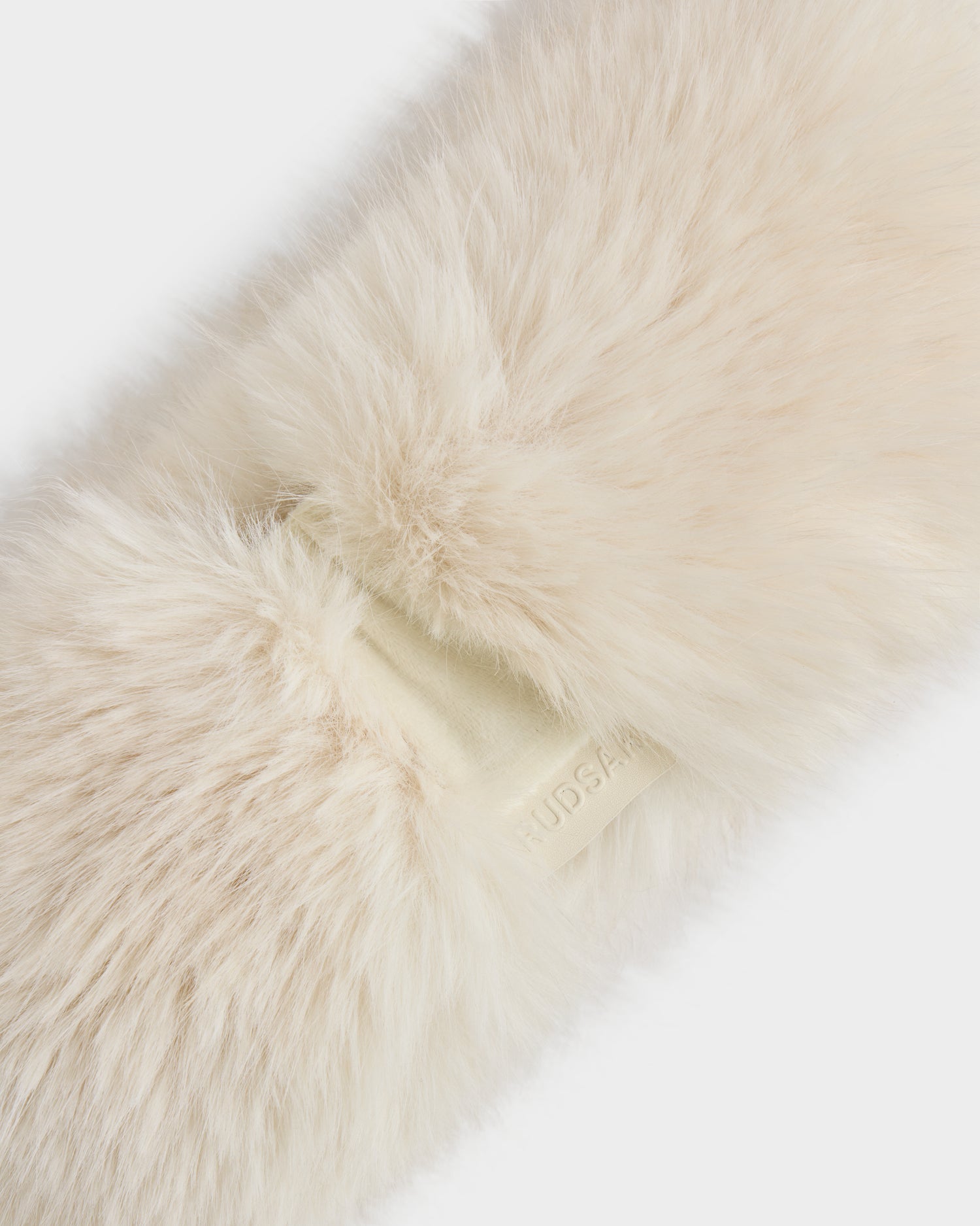 Close-up of the ARLETTE - 8425544 Vanilla women’s faux fur headband by Rudsak, a fluffy cream-colored winter accessory with a small, embossed tag partially visible.