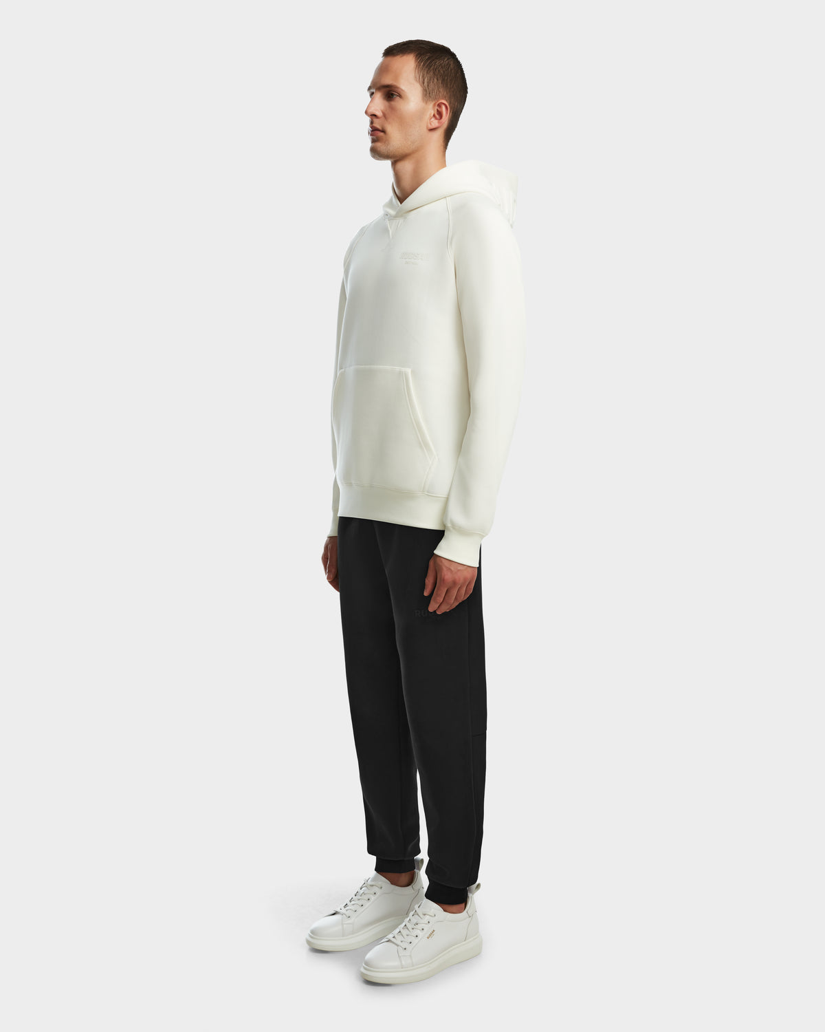 A man in a white Rudsak BARRY - 9524011 Iceland M hoodie stands confidently, highlighting the relaxed and modern style of this unisex piece.