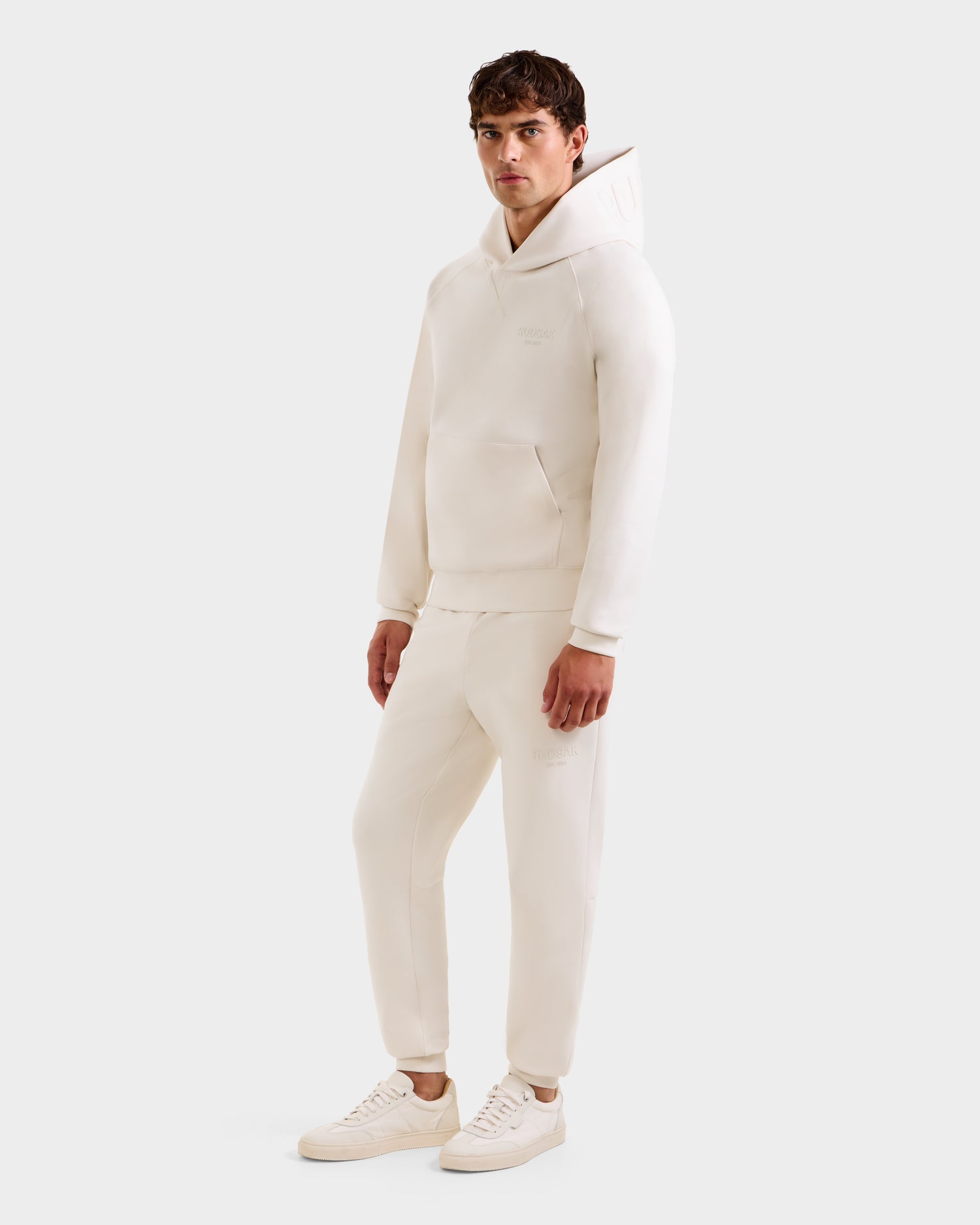 A man wears the Rudsak BARRY - 9524011 Vanilla M oversized hoodie and sweatpants set with white sneakers, posing against a plain light background.