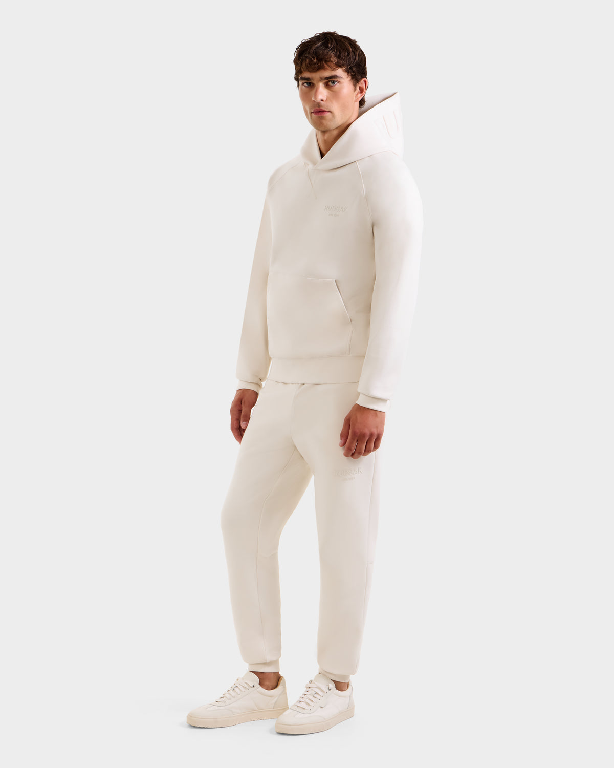 A man wears the Rudsak BARRY - 9524011 Vanilla M oversized hoodie and sweatpants set with white sneakers, posing against a plain light background.