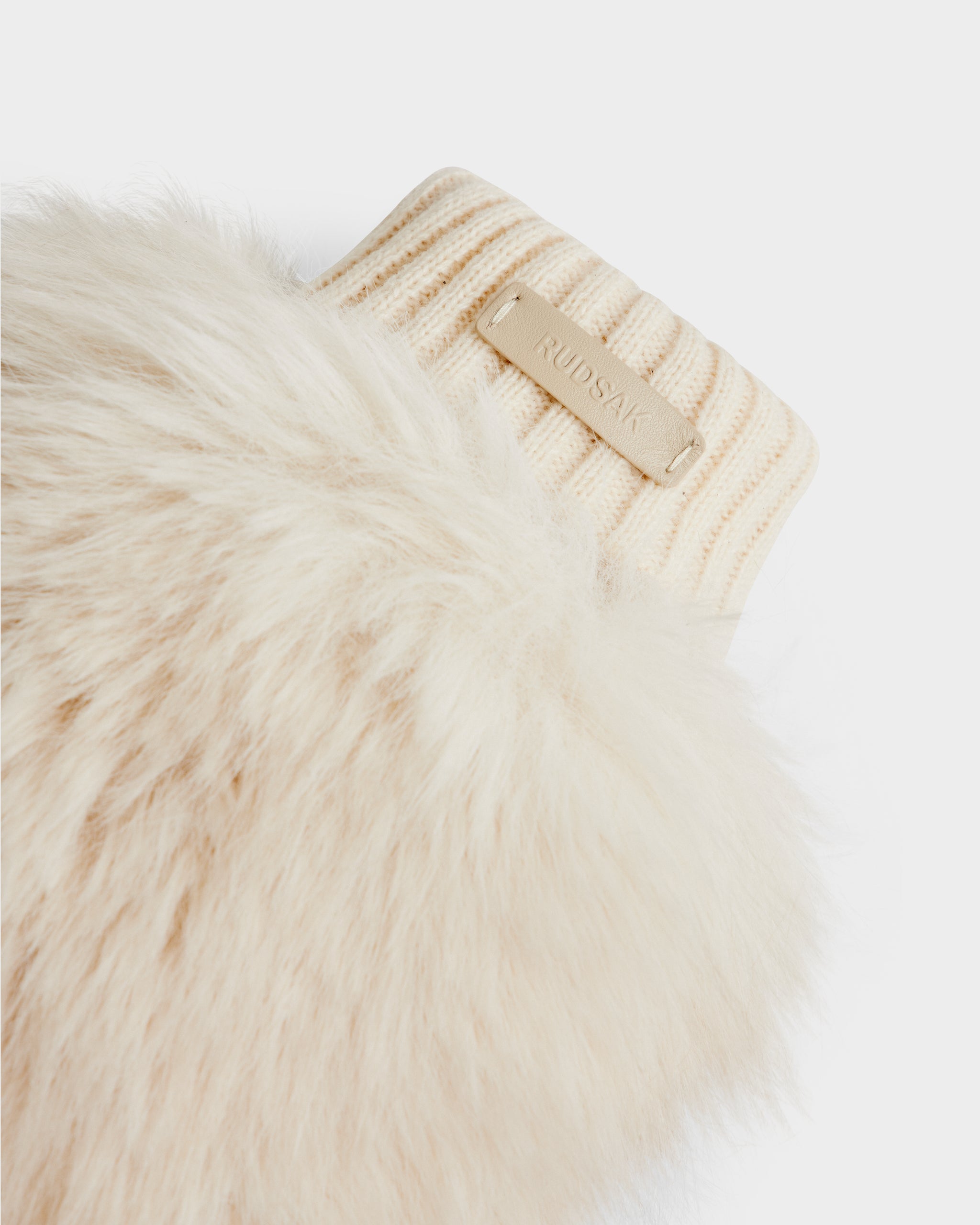 Close-up of BELLA - 8425006 Vanilla by Rudsak: cream ribbed knit cuff joins soft beige faux fur, accented with a small Rudsak tag—an elegant touch on these cozy mittens, perfect as après-ski accessories.