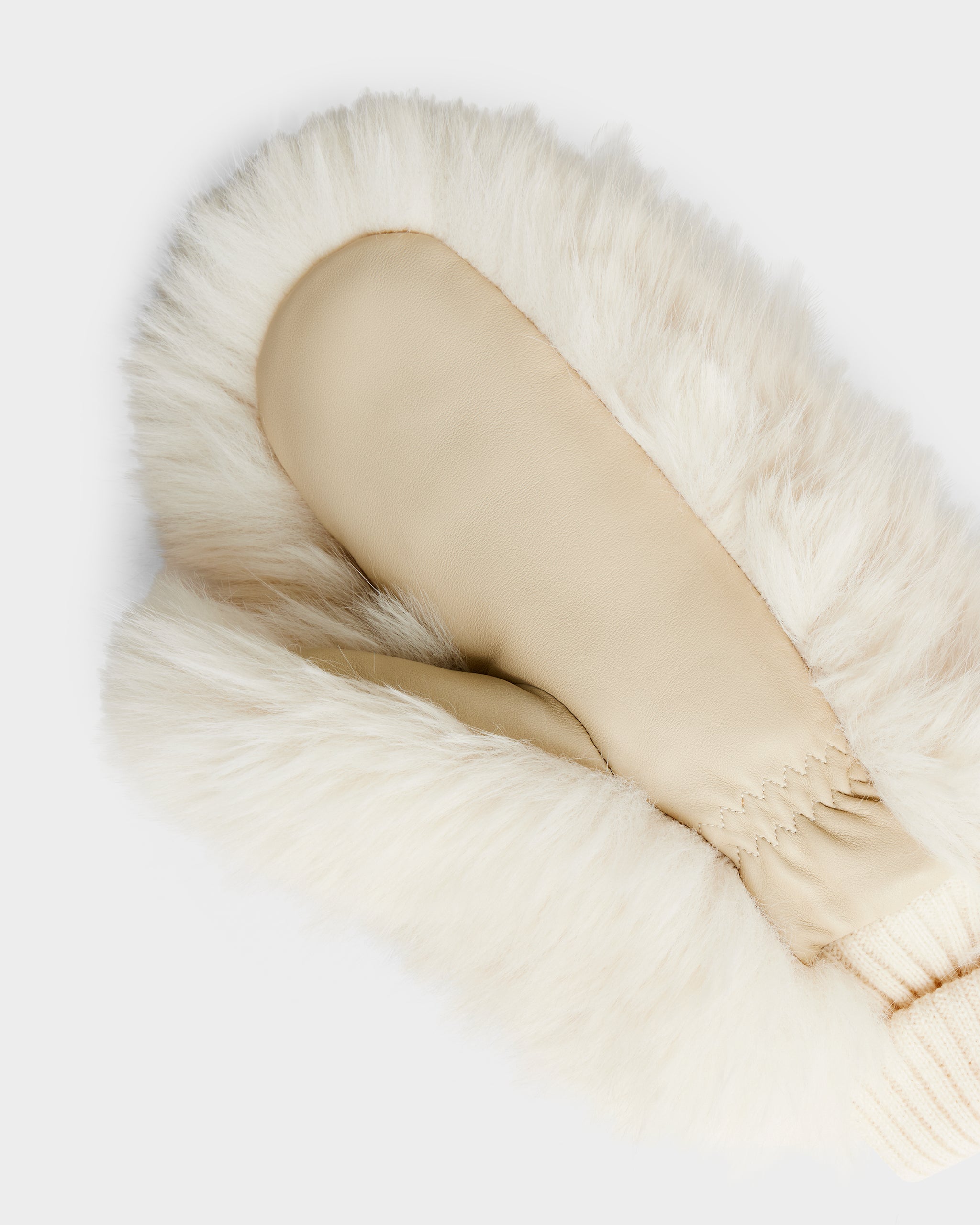 The BELLA - 8425006 Vanilla mitten by Rudsak, in beige leather with a ribbed knit cuff, is shown atop fluffy white faux fur, photographed from above against a plain white background.