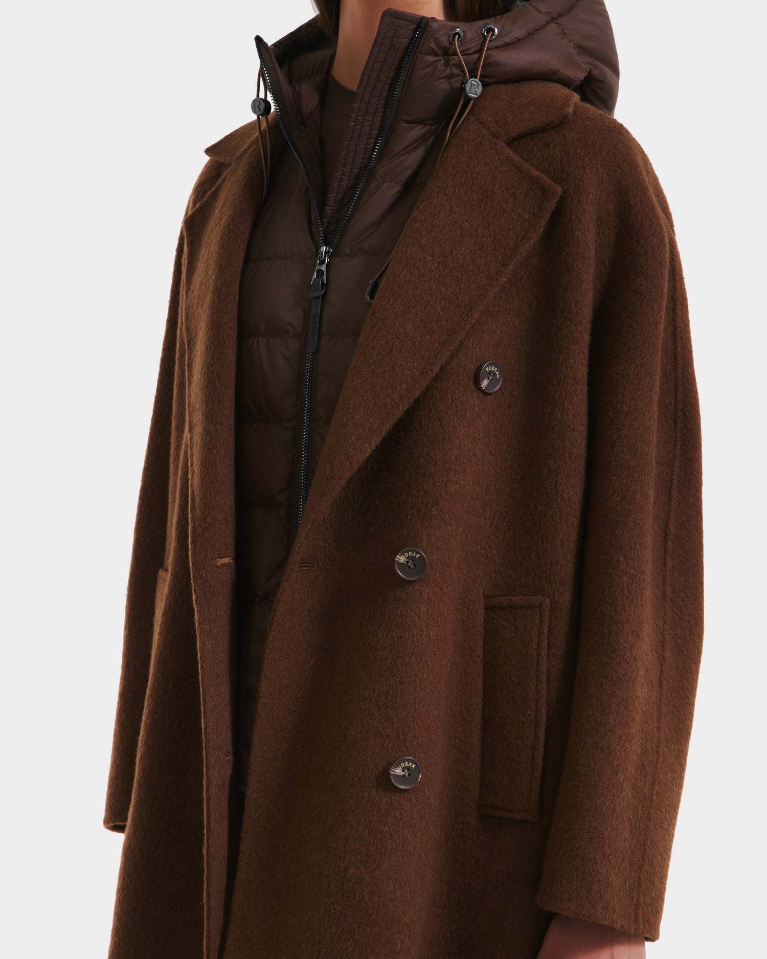A person wears the Rudsak BETHANY - 8125625 Mocha double-breasted coat over a brown quilted puffer jacket, creating a modern 3-in-1 silhouette, shown from shoulders to mid-thigh against a white background.