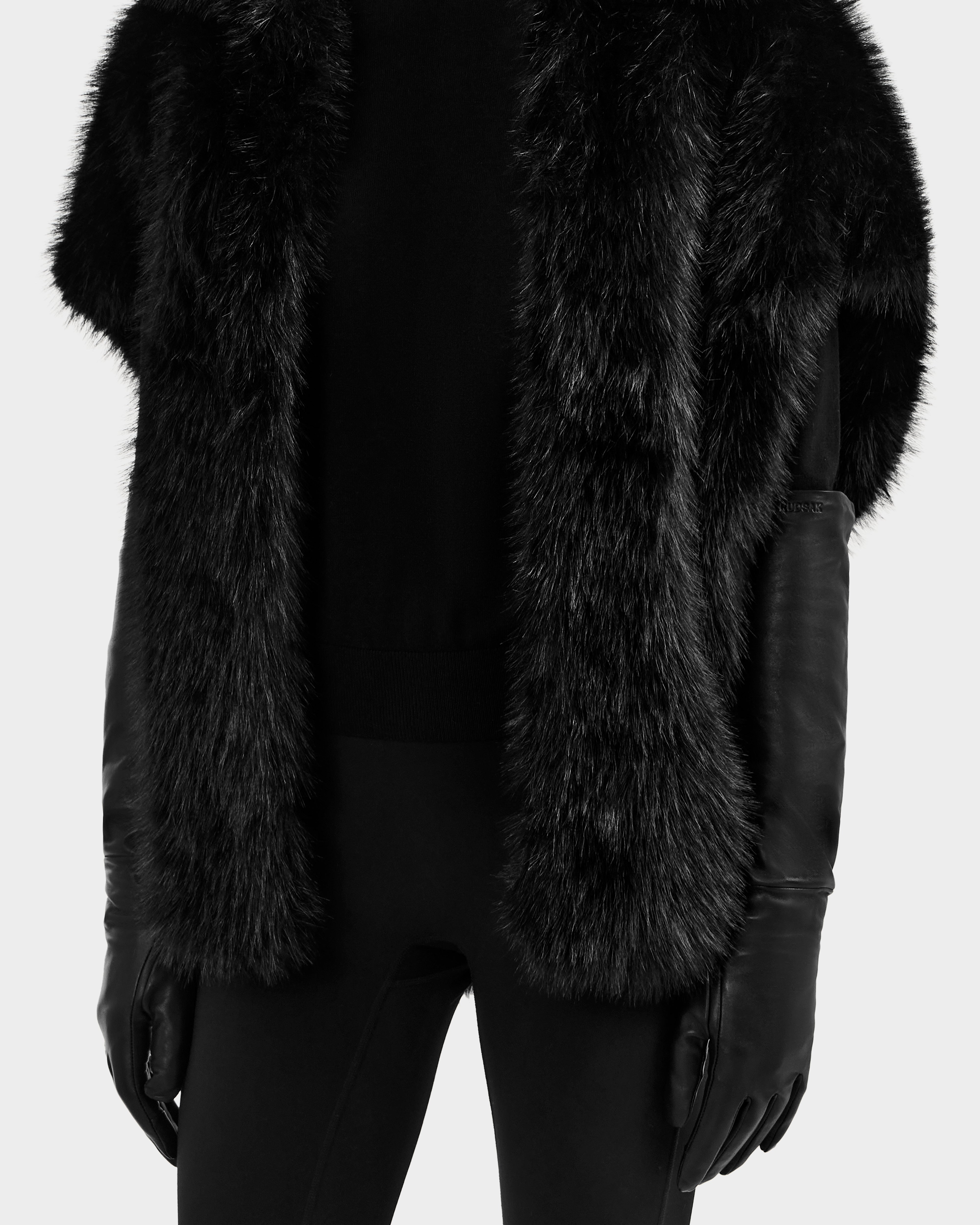 A model wears the Rudsak BLAKE - 8425542 Black fur vest with a black long-sleeve top, black pants, and long women's leather gloves, shown from shoulders to mid-thigh against a plain background.
