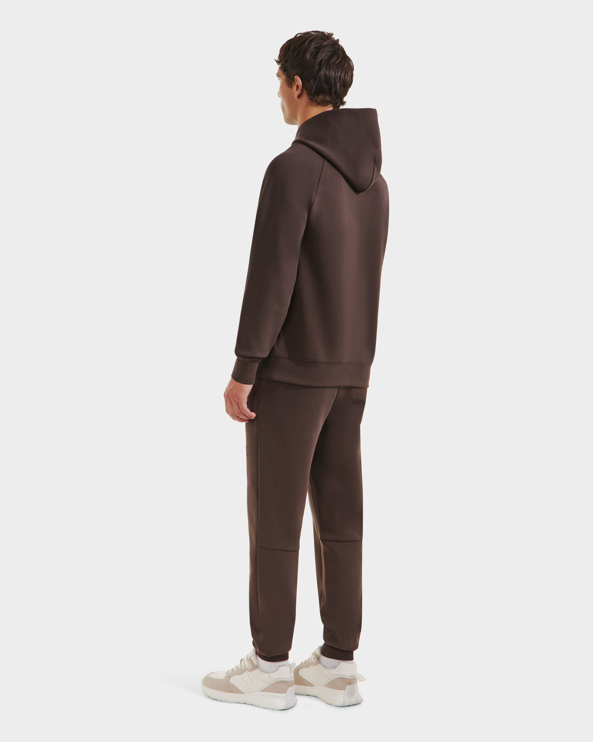 A man faces away, wearing the Rudsak BRIAR - 9525001 Espresso M unisex hoodie and matching brown sweatpants, made from a premium cotton blend with white sneakers, set against a plain white background.