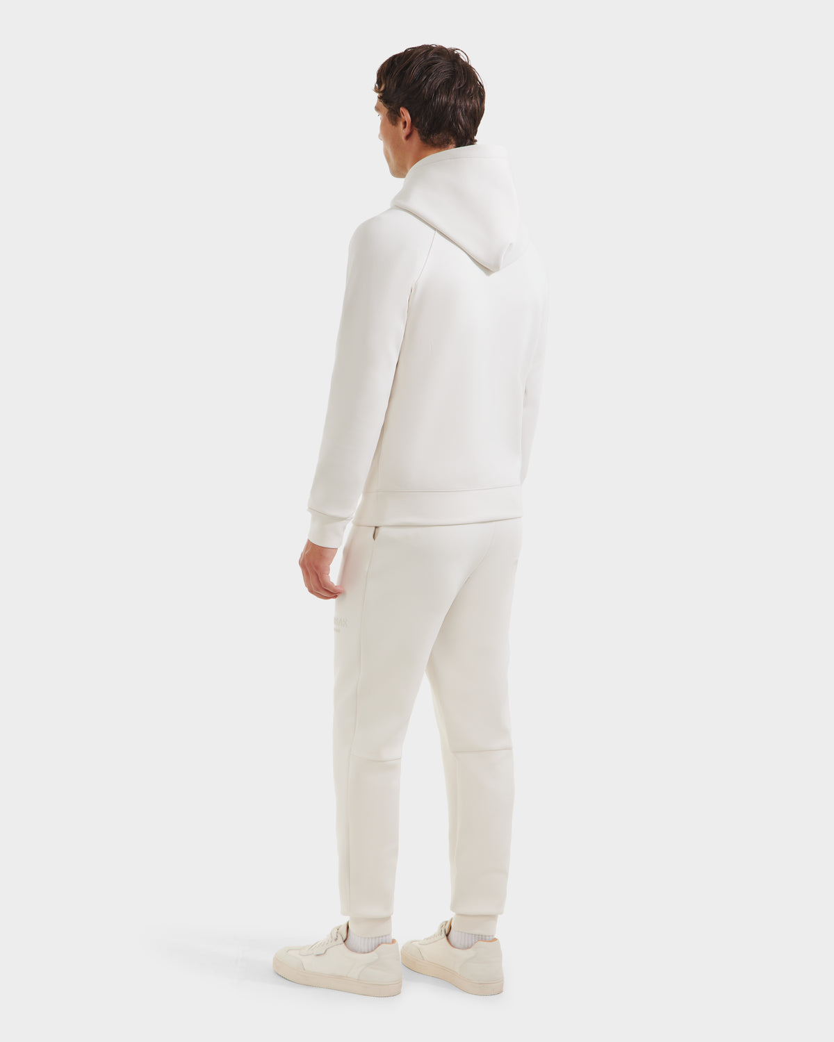 A person stands facing away, wearing the Rudsak BROOKLYN - 6525593 Vanilla mens hoodie and matching sweatpants with white sneakers, set against a plain white background.