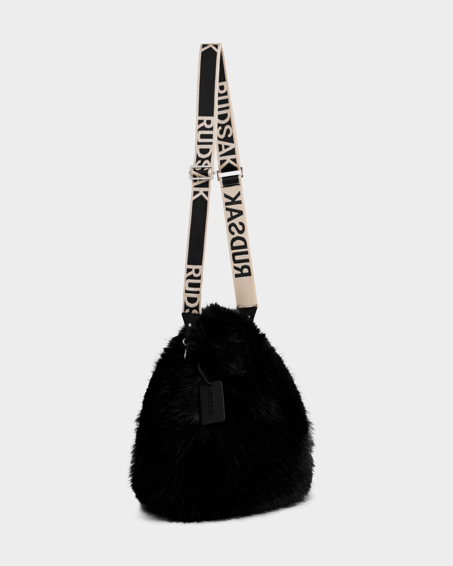 The Rudsak CABAS - 8325545 Black is a black, triangular faux fur mini tote with a beige and black strap featuring "RUDSAK" in bold letters and a black tag near the strap.