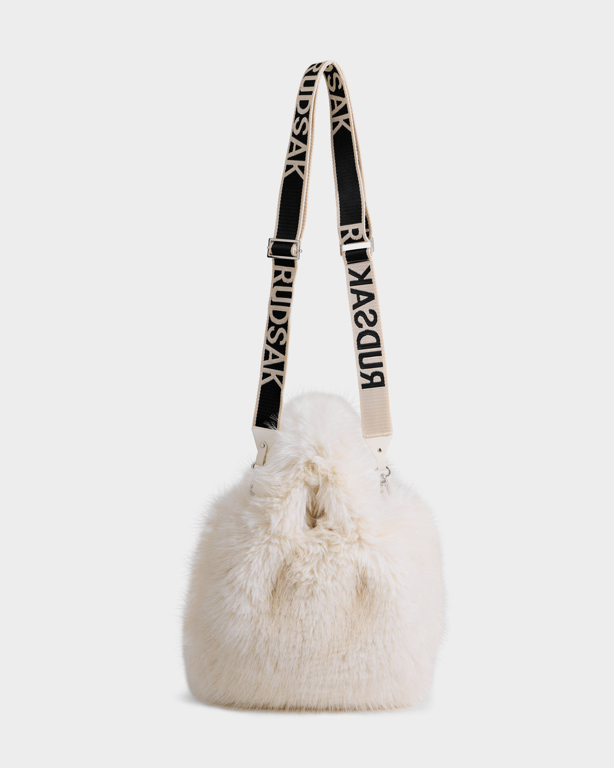 The Rudsak CABAS - 8325545 Vanilla is a white faux fur mini tote with a wide adjustable black strap featuring bold RUDSAK lettering—a chic statement for winter outfits, showcased on a plain white background.