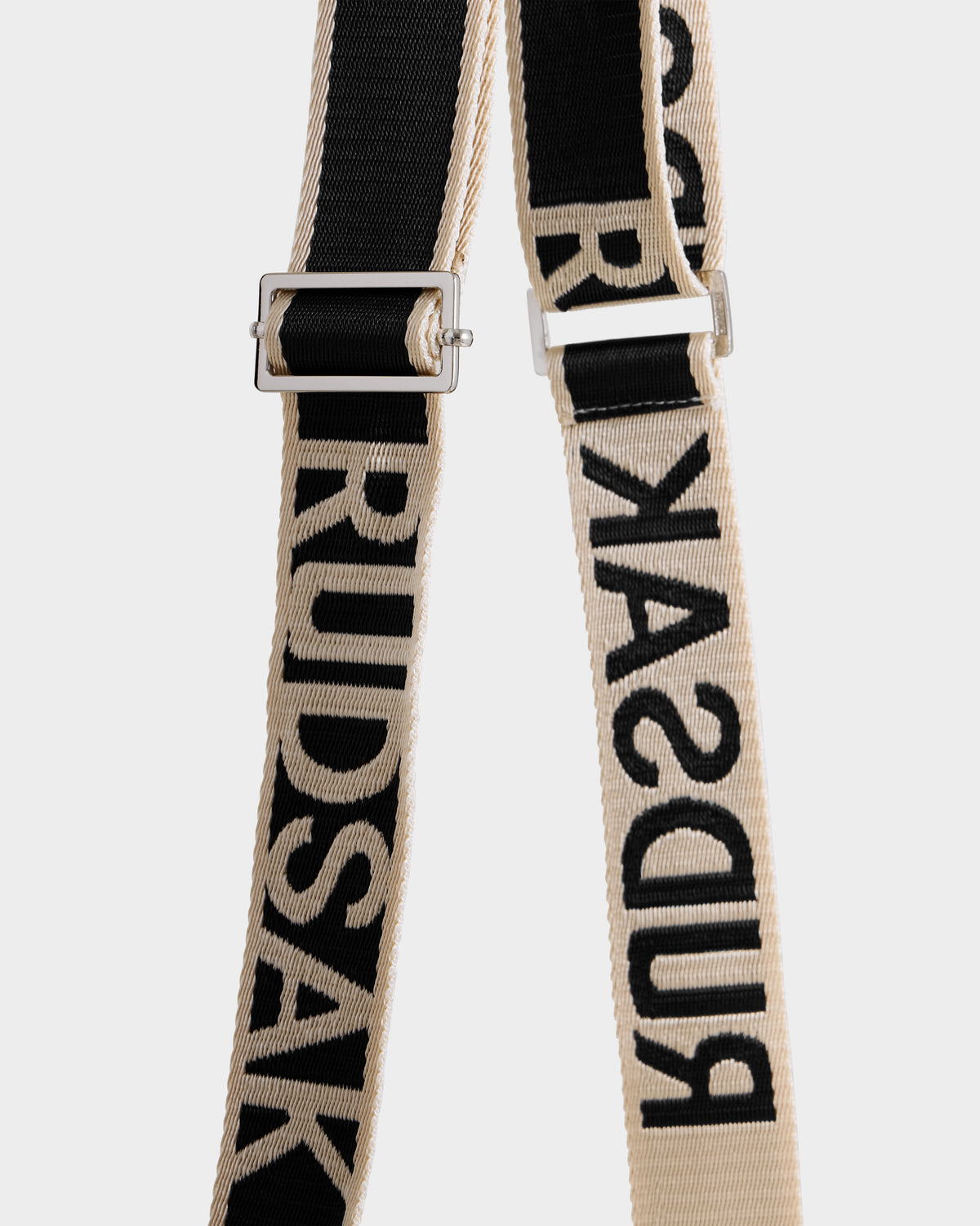 Two adjustable fabric straps, one black and one beige, with bold Rudsak branding and metal hardware. The CABAS - 8325545 Vanilla is a statement accessory—perfect for winter layers or pairing with a faux fur mini tote.