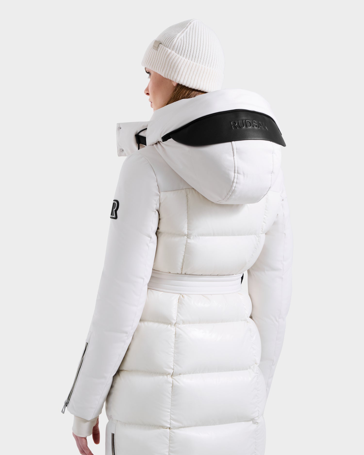 A person is shown from the back against a plain light background wearing Rudsak's CALI H - 8125614 Vanilla women’s long down parka with removable hood, high-loft 800+ fill power down, and a white knit beanie.