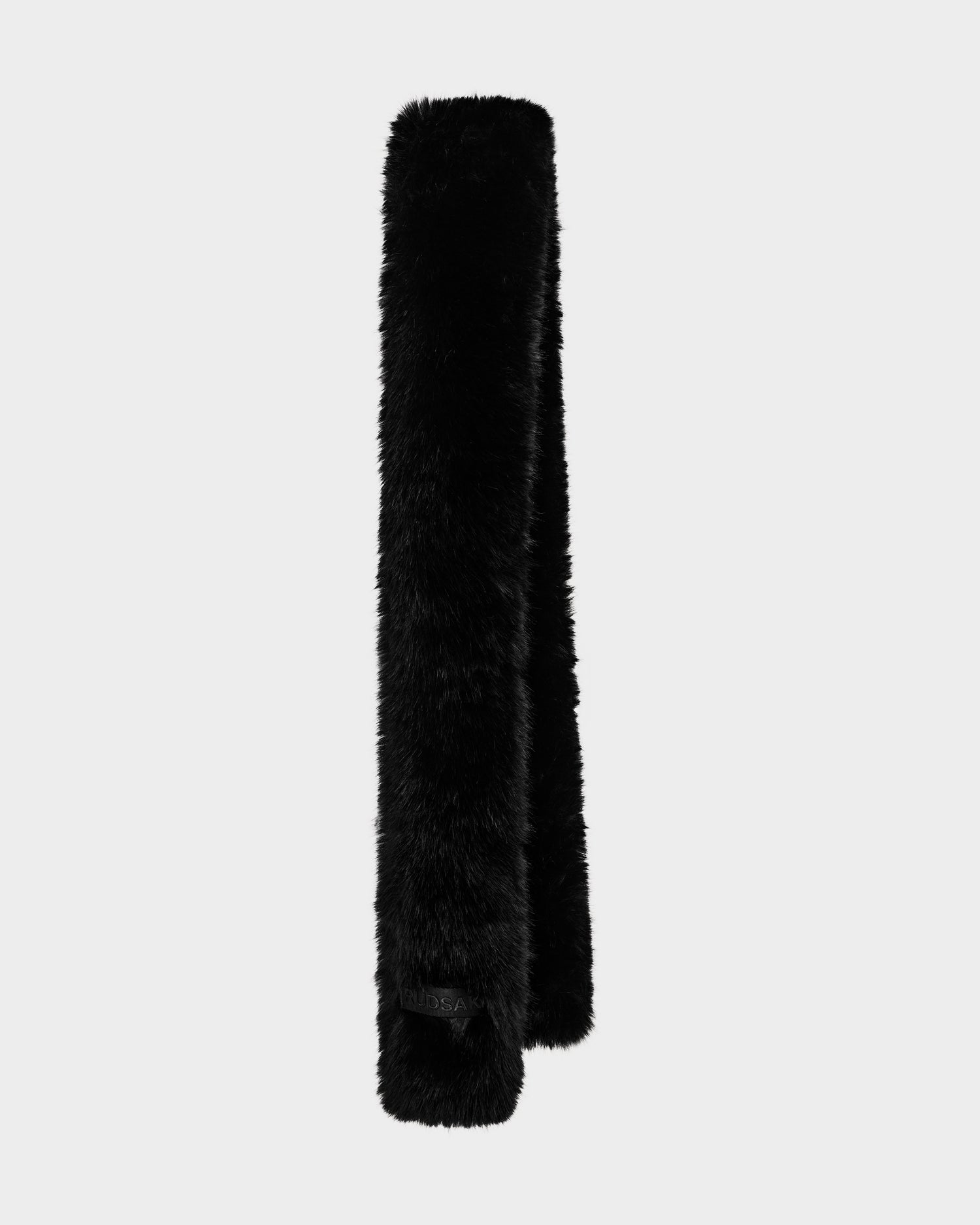 The CARMY - L425534 Black by Rudsak is a women’s faux-fur scarf shown against a light gray background. Rectangular with rounded edges, it appears soft and plush—an ideal cold-weather accessory for warmth.
