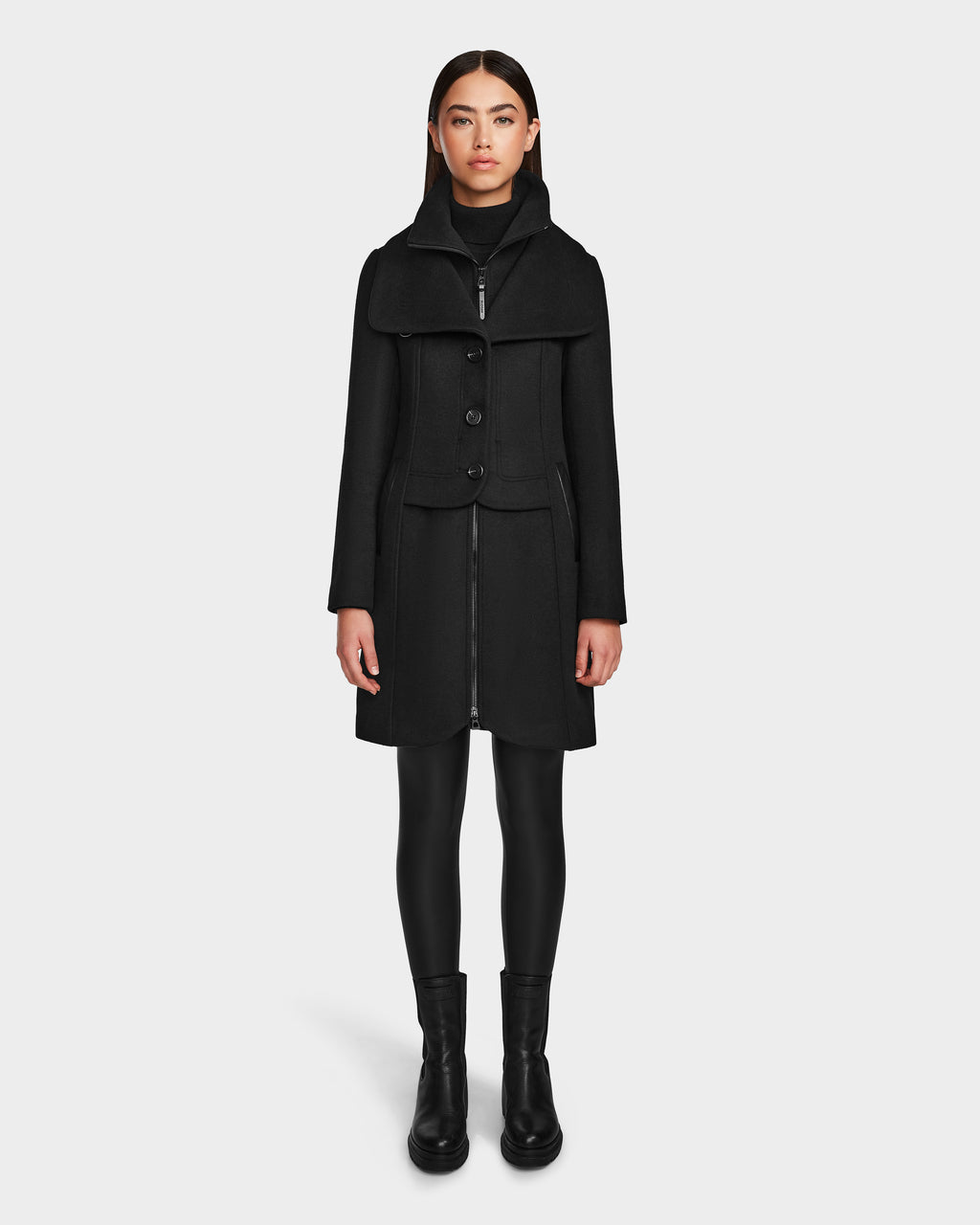 A woman faces forward wearing the Rudsak CAROLINE - L124543 Black knee-length premium wool blend coat, styled with a black turtleneck, leggings, and ankle boots against a plain white background.