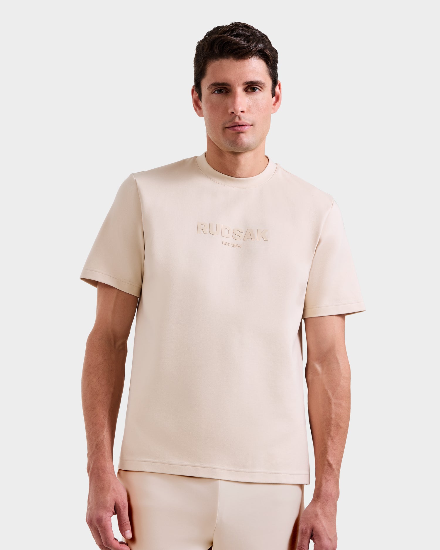 A man with short dark hair wears a Rudsak CASEY - 6525037 Vanilla T-shirt, subtly embossed on the front and paired with matching pants, standing facing forward against a plain white background.