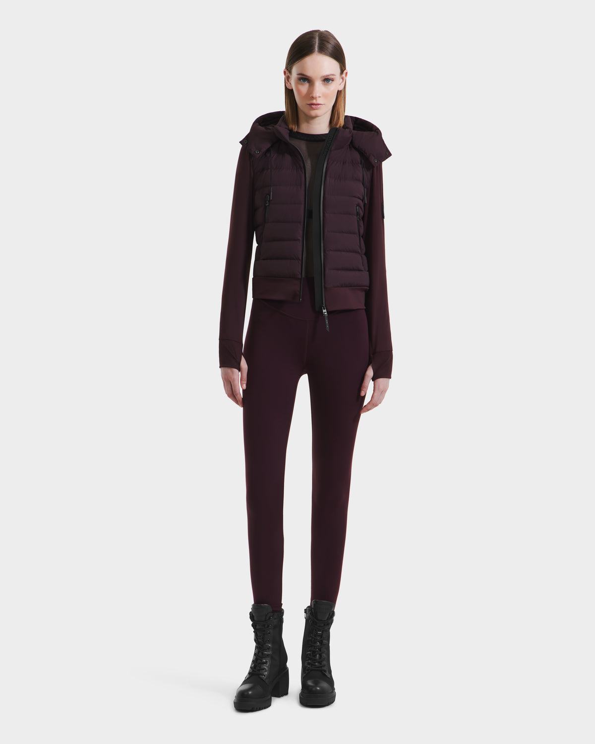A woman with straight brown hair models the Rudsak CASSA - 8125057 Bordeaux fitted jacket and pants set with a matching puffer vest and black lace-up boots, standing against a plain white background.