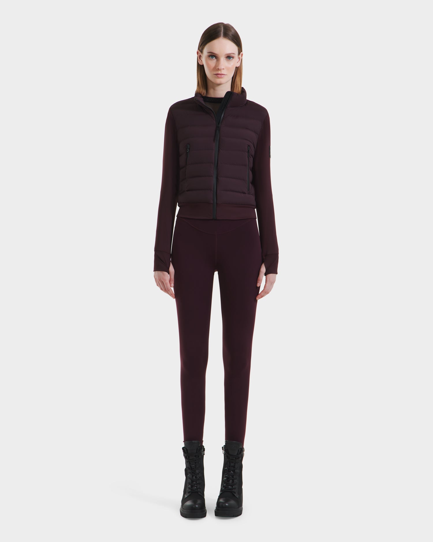 A woman faces forward against a white background, wearing the Rudsak CASSA - 8125057 Bordeaux fitted, lightweight cropped women’s jacket with quilted panels and matching leggings—ideal for transitional weather.