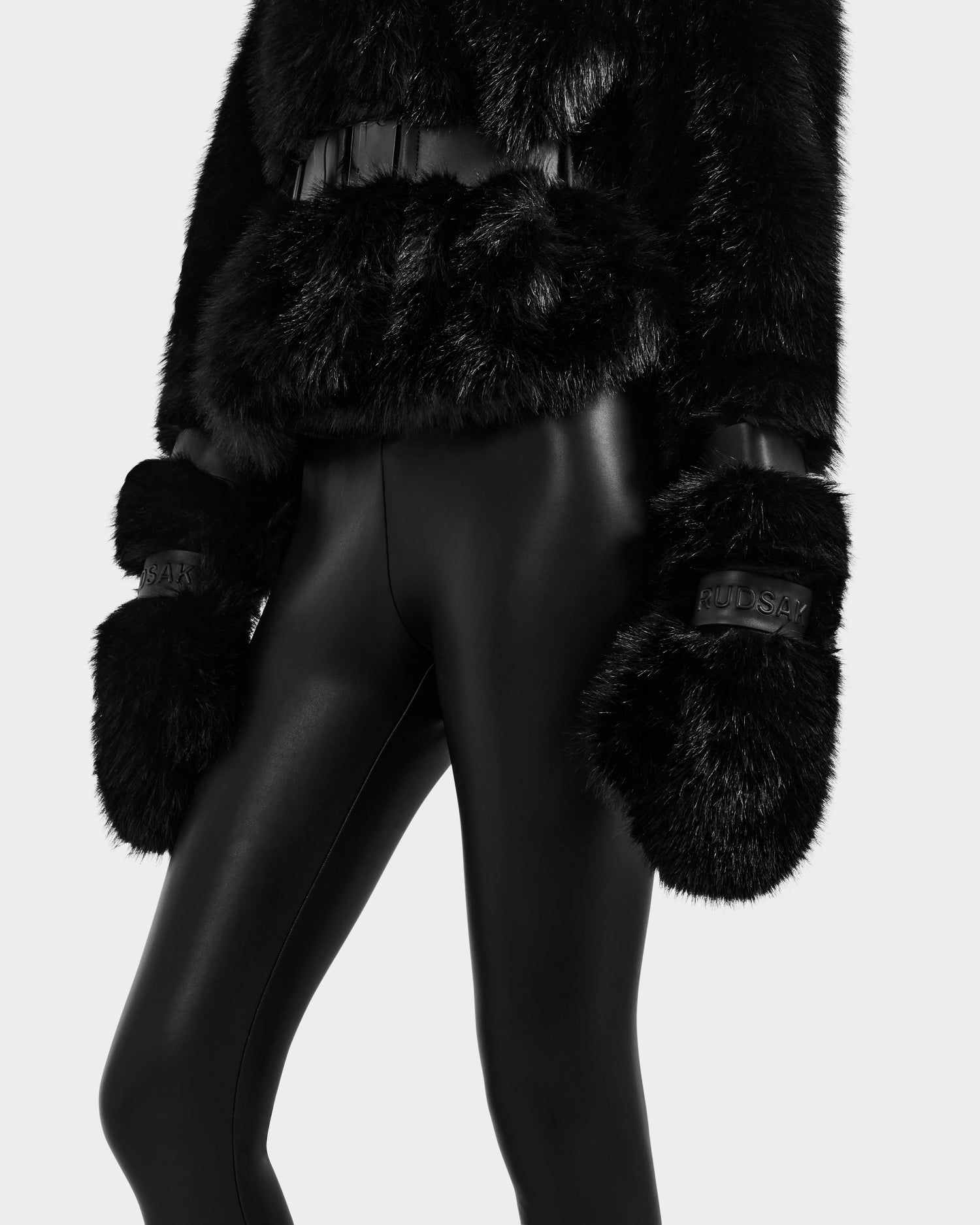 A person models the Rudsak CHLOE - 8125619 Black faux fur jacket, paired with black faux fur mittens and shiny black leggings, shown from shoulders to thighs against a neutral background—ideal winter fashion inspiration.