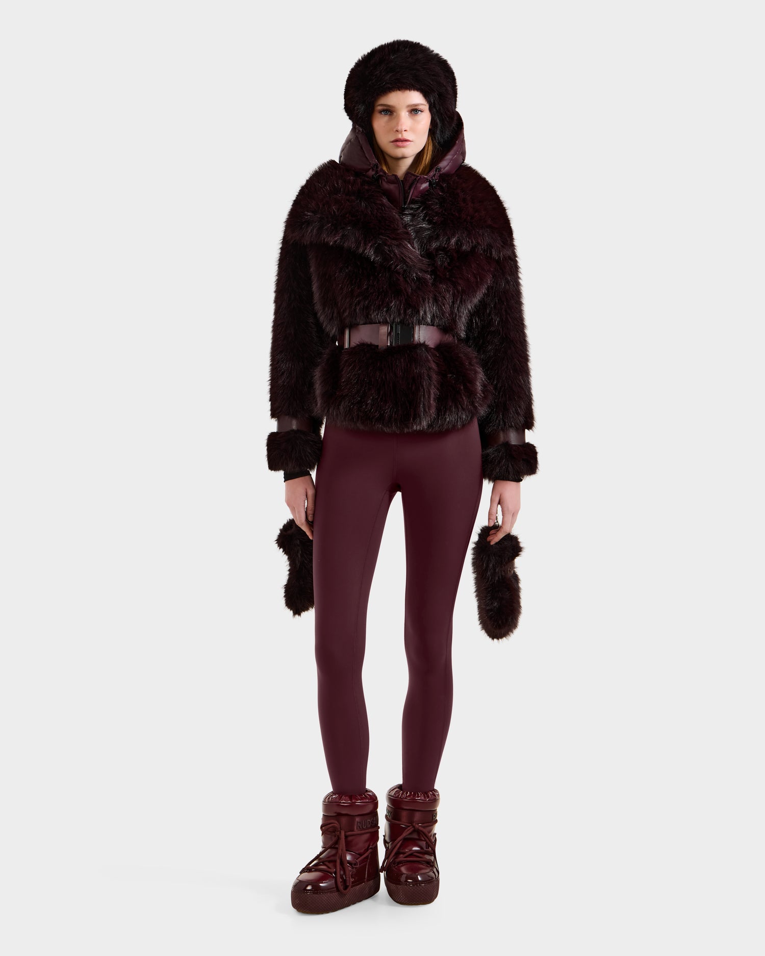 A person wears the CHLOE - 8125619 Bordeaux faux fur jacket by Rudsak, with matching leggings and chunky burgundy boots, standing against a white background—an ideal look to elevate your winter wardrobe.