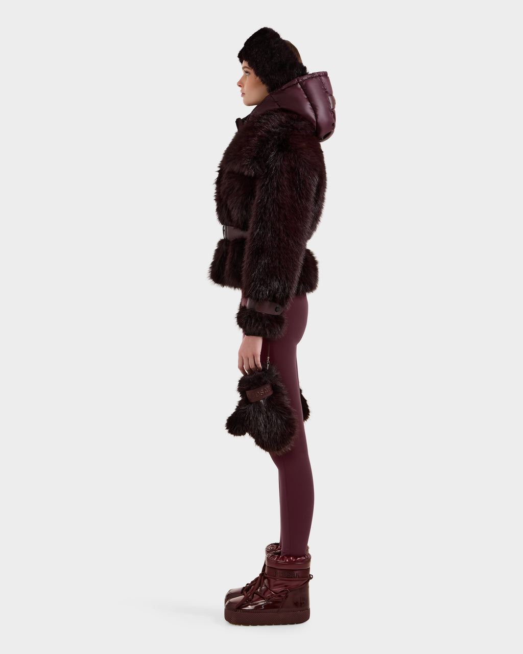 A person in side profile models the CHLOE - 8125619 Bordeaux faux fur jacket by Rudsak with matching pants, fur-trimmed gloves, a hat, and boots—an elegant winter look—against a plain white background.