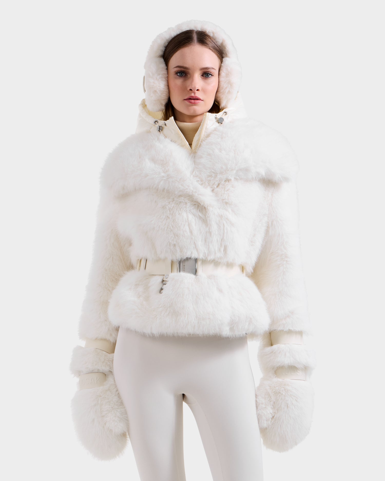A woman models the Rudsak CHLOE - 8125619 Iceland women's faux fur jacket with a belt, paired with matching mittens and off-white fitted pants, standing against a light background to showcase cozy winter style.