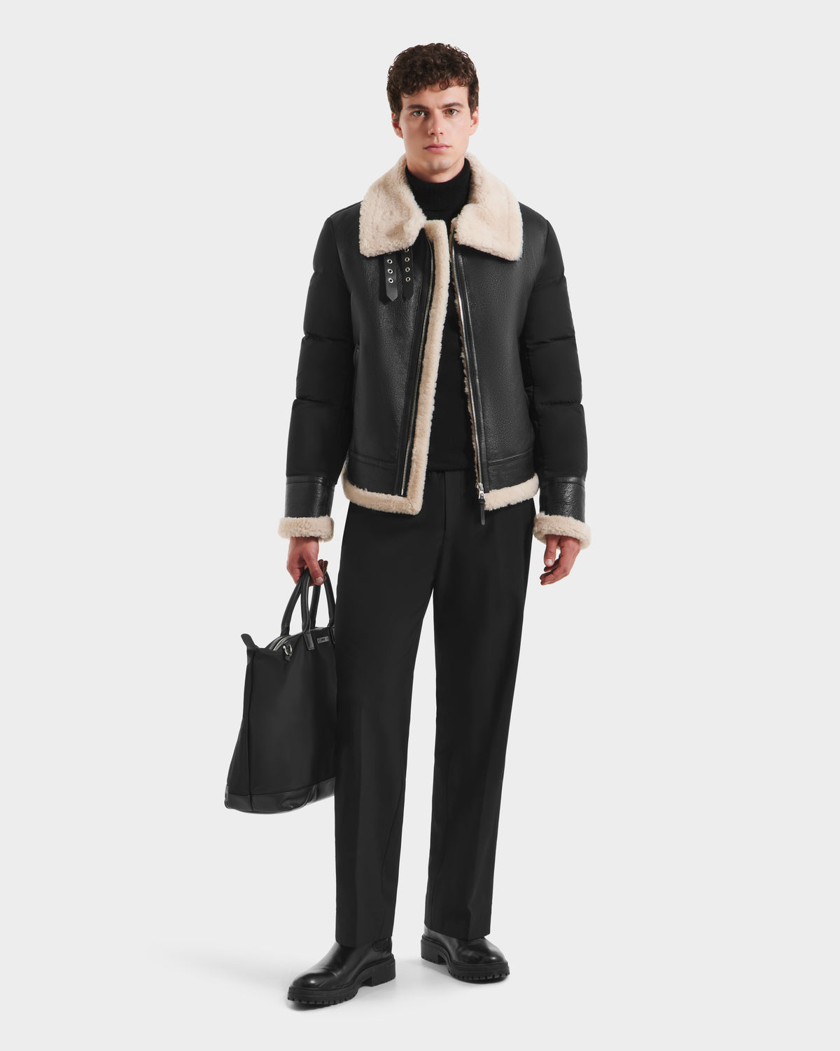 A man in a black Rudsak CLAYTON - 6125501 down puffer jacket and black pants is holding a bag.