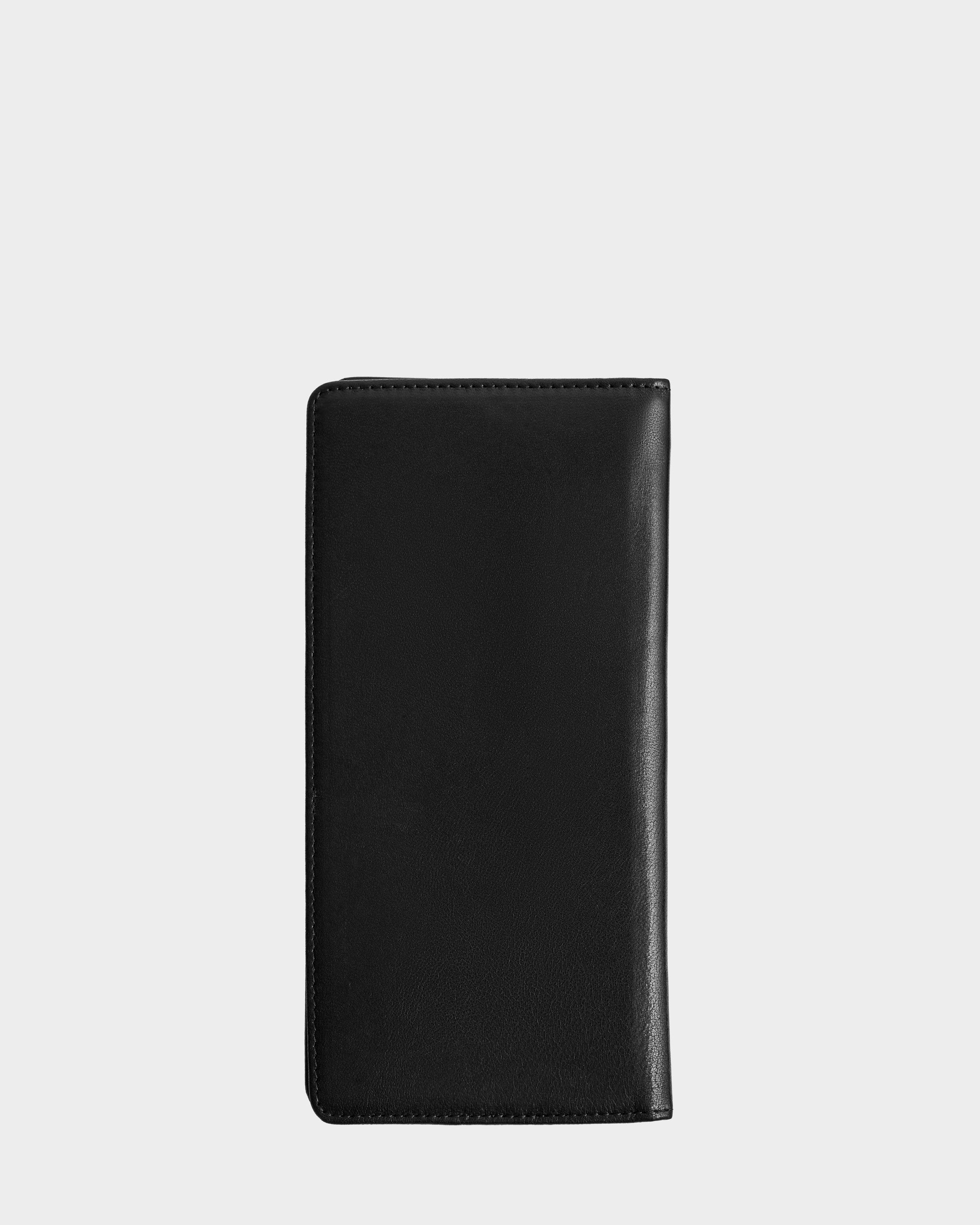 The Rudsak CLEO - 9425522 Black, a sleek unisex leather passport holder or travel wallet, stands upright against a plain light gray background.