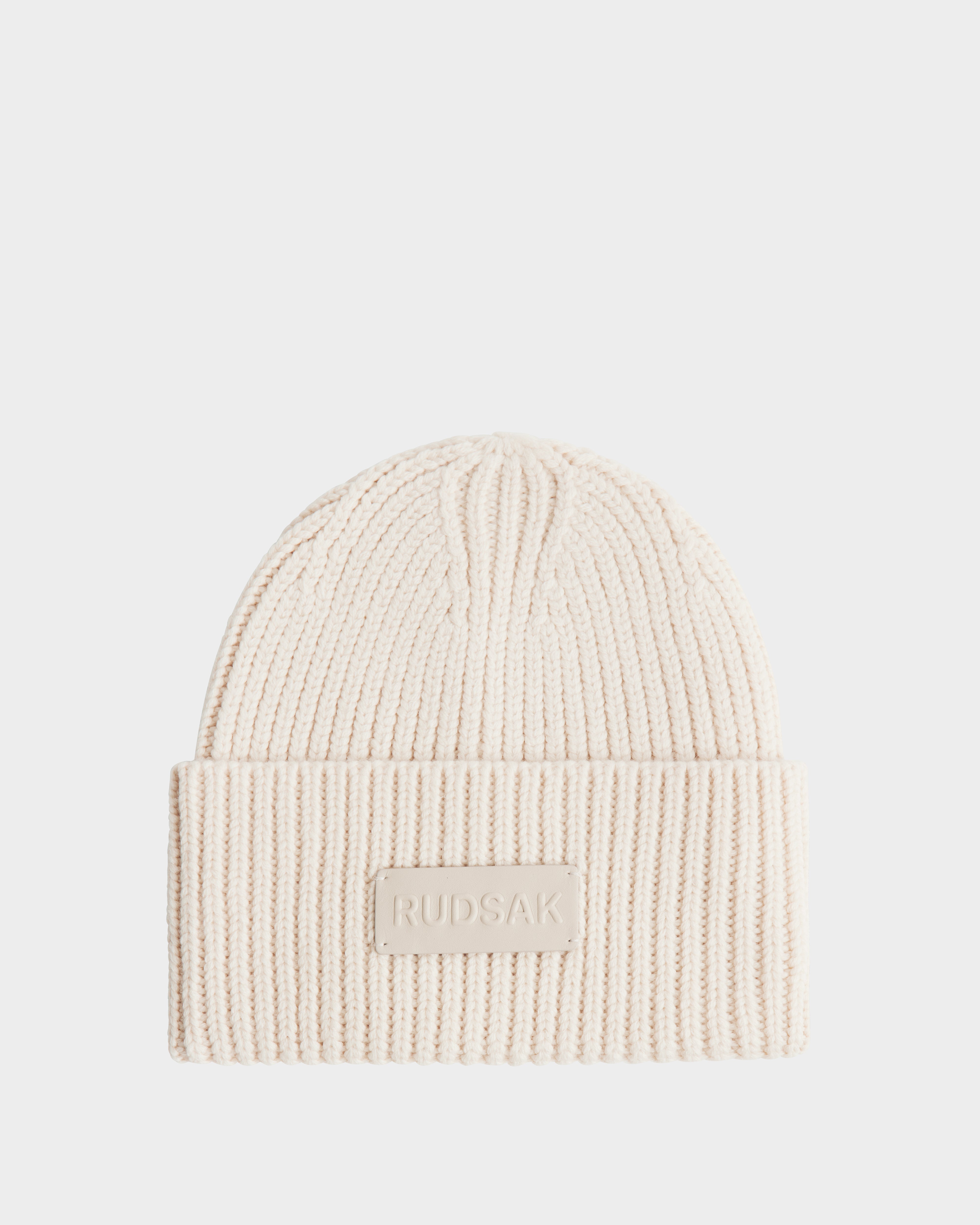 The COLIN - 9424518 Vanilla beanie by Rudsak is a cream ribbed merino wool knit with a folded brim and a front patch featuring the embossed RUDSAK name. This cozy unisex beanie is shown on a plain white background.