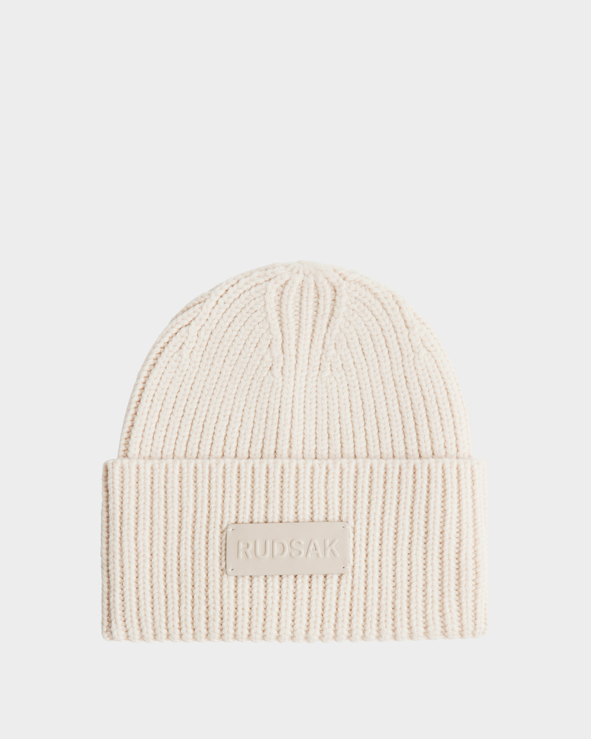The COLIN - 9424518 Vanilla beanie by Rudsak is a cream ribbed merino wool knit with a folded brim and a front patch featuring the embossed RUDSAK name. This cozy unisex beanie is shown on a plain white background.
