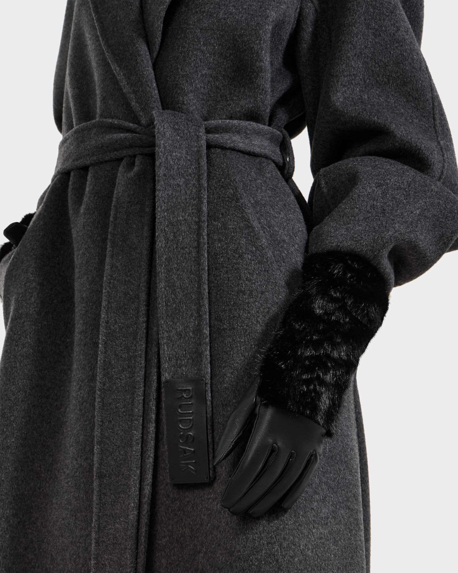 A person wears a dark grey belted coat with a visible Rudsak label, completing the look with elegant black faux fur COVE - 8425533 gloves by Rudsak.