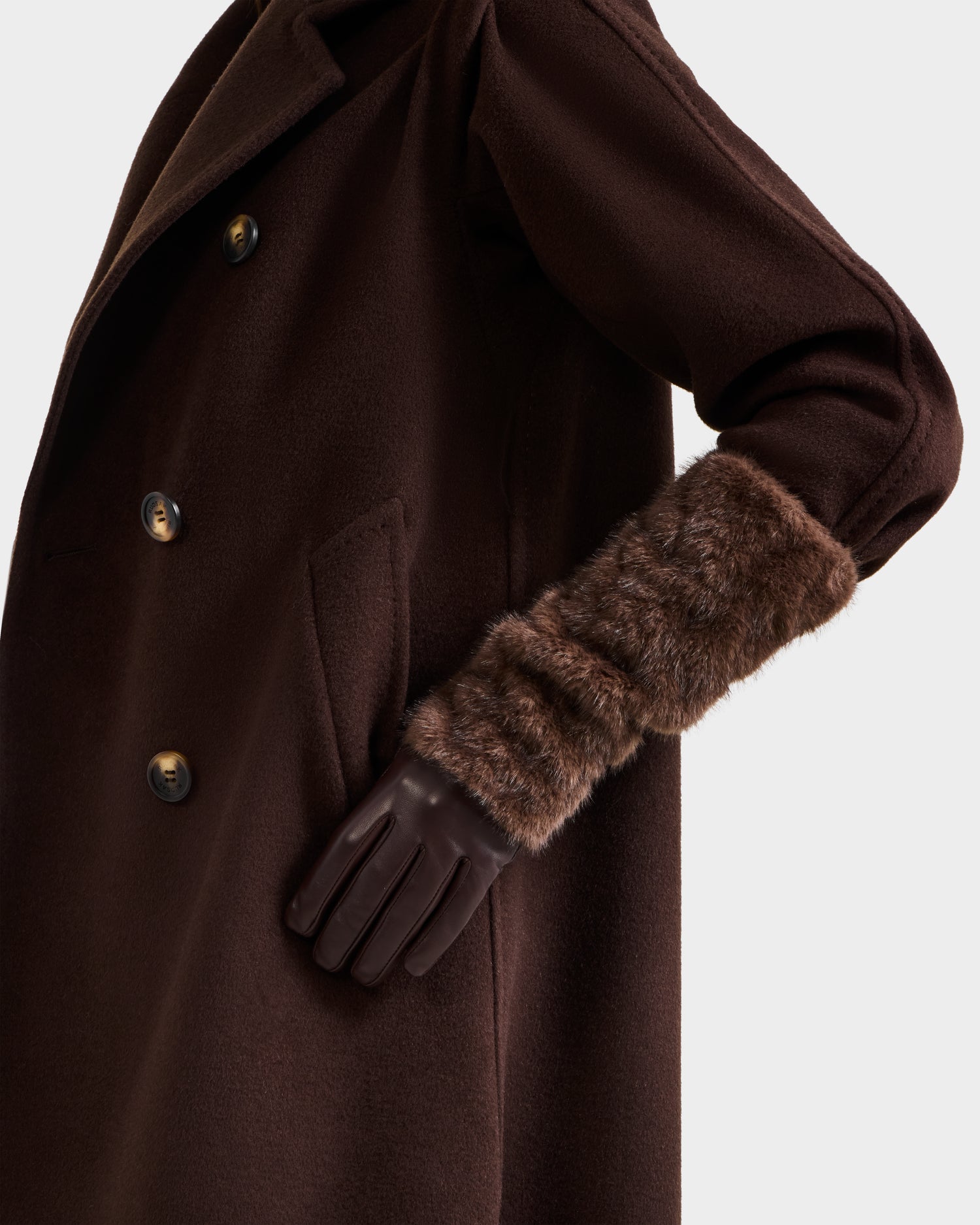 A person models the Rudsak COVE - 8425533 Mocha dark brown coat with large buttons and faux fur cuffs, paired with touchscreen-compatible dark brown gloves, shown from the shoulders down with one hand in the coat pocket.