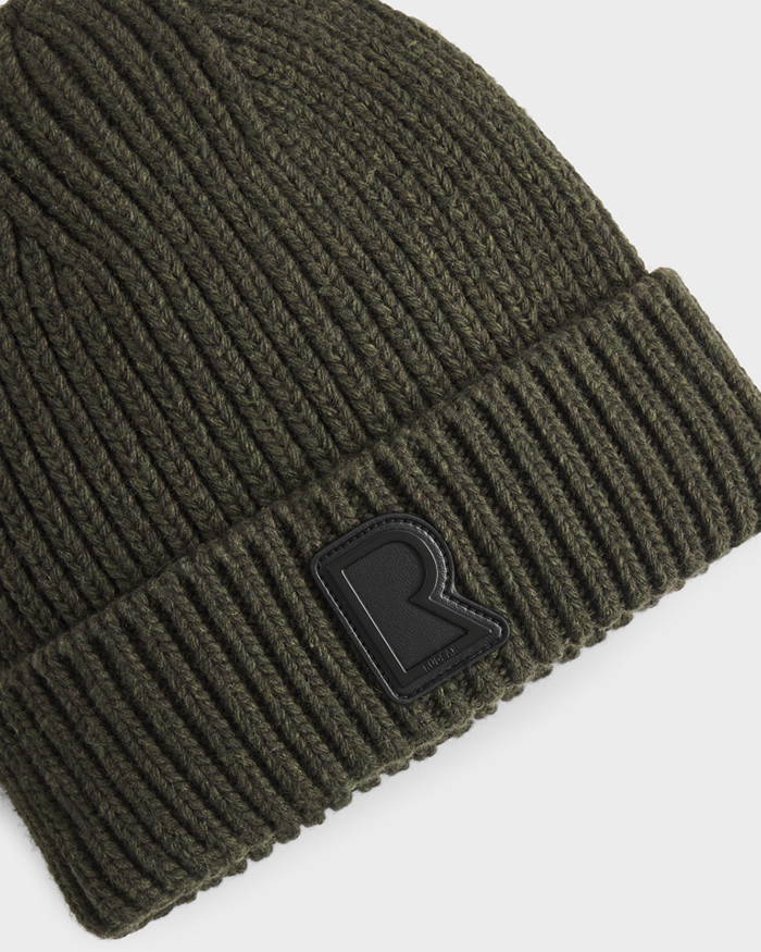 A close-up of the CYBELLE - 9424504 Dark Olive unisex knit hat by Rudsak, featuring ribbed wool blend fabric and a black R logo patch on the folded brim—a signature winter accessory.